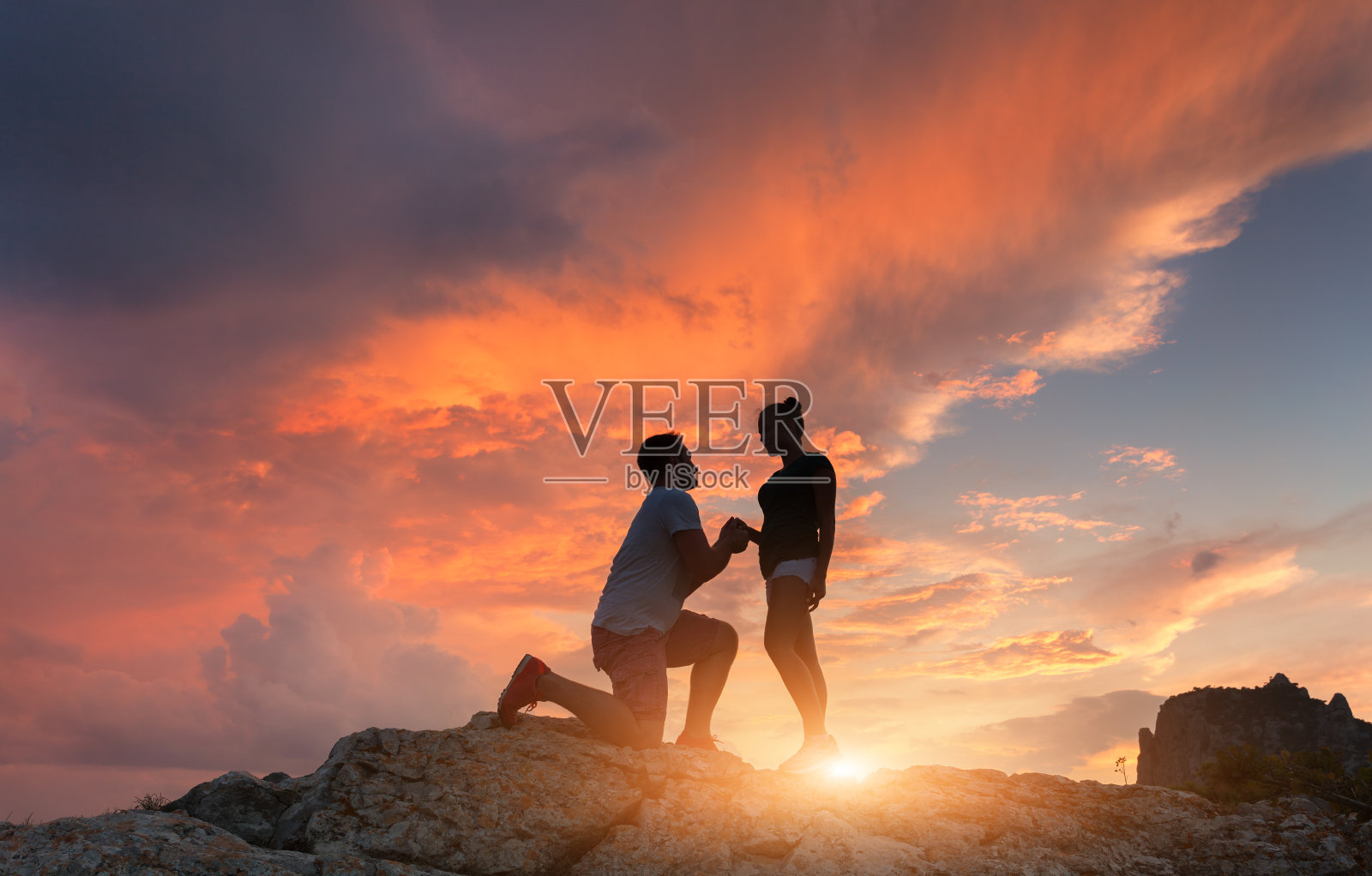 日落时分，山顶上一个男子向女友求婚的剪影。色彩斑斓的天空映衬着恋人的剪影。夫妇。人的关系。一些旅行照片摄影图片