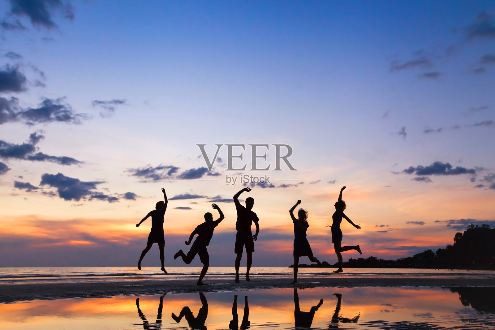 日落时分，一群快乐的人在海滩上跳跃照片摄影图片