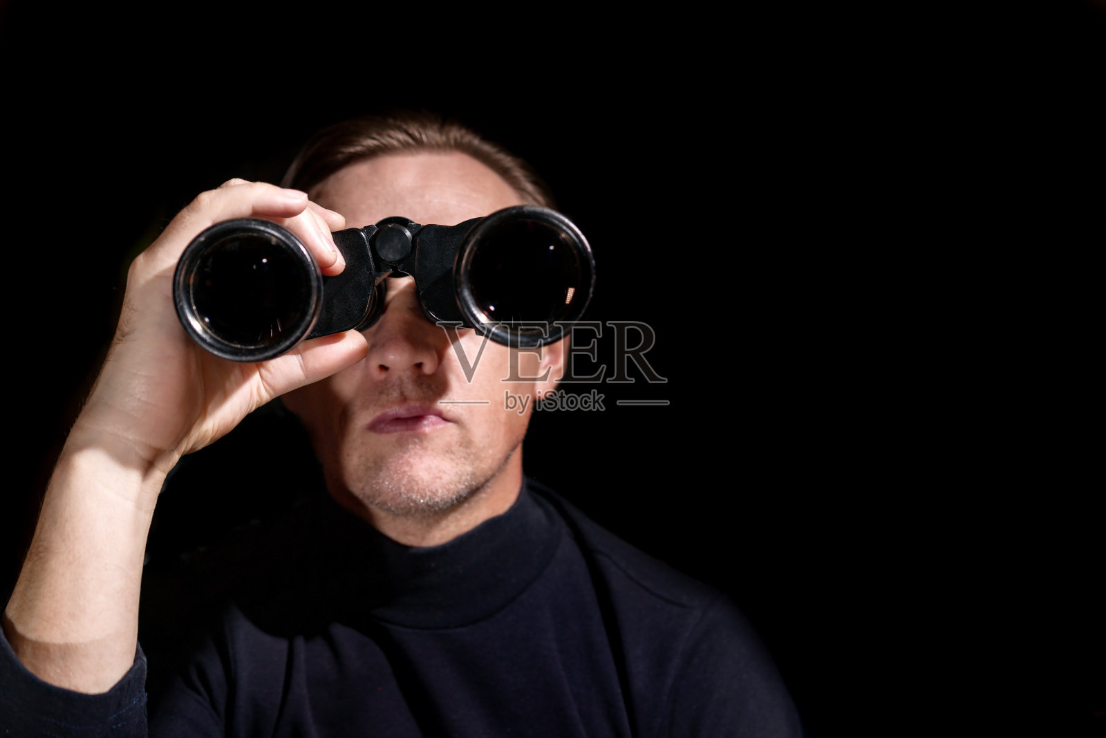 在黑暗的背景下，一名男子用双筒望远镜看东西照片摄影图片