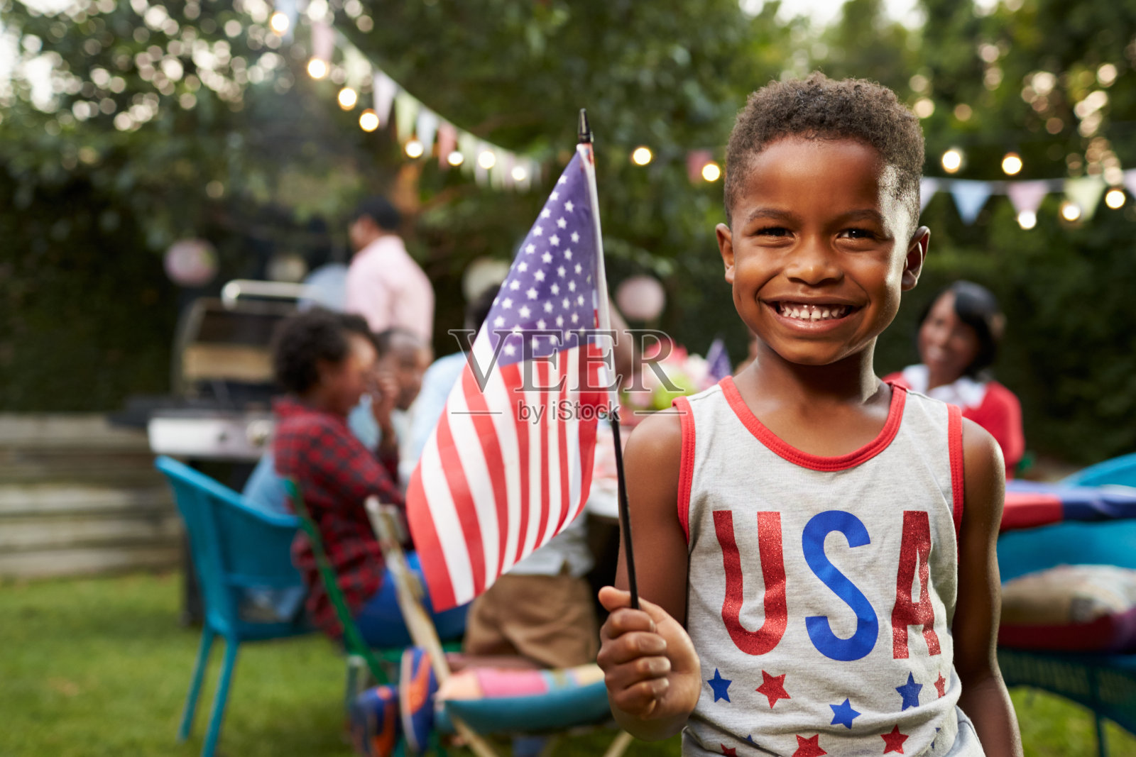 一个年轻的黑人男孩在7月4日的家庭花园举着旗帜照片摄影图片