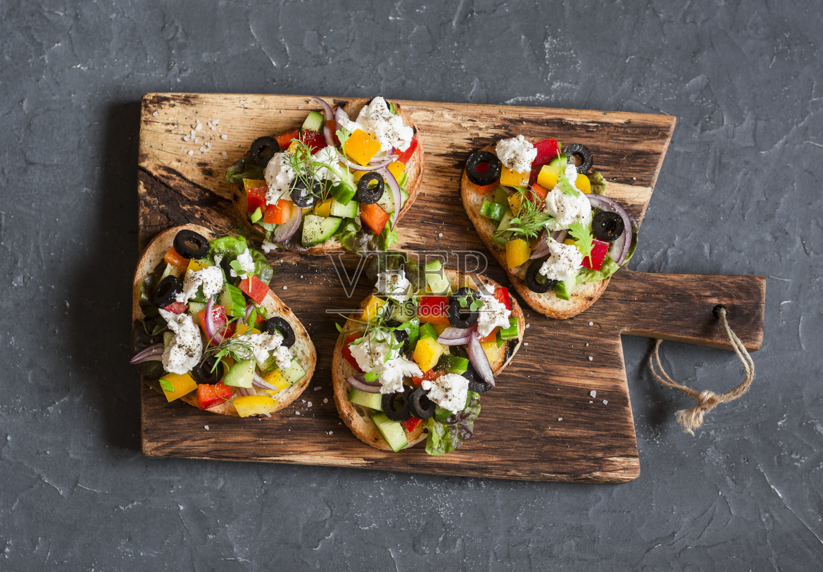 希腊沙拉风格的意式烤面包放在木砧板上，深色背景，俯视图。美味的开胃酒或小吃照片摄影图片
