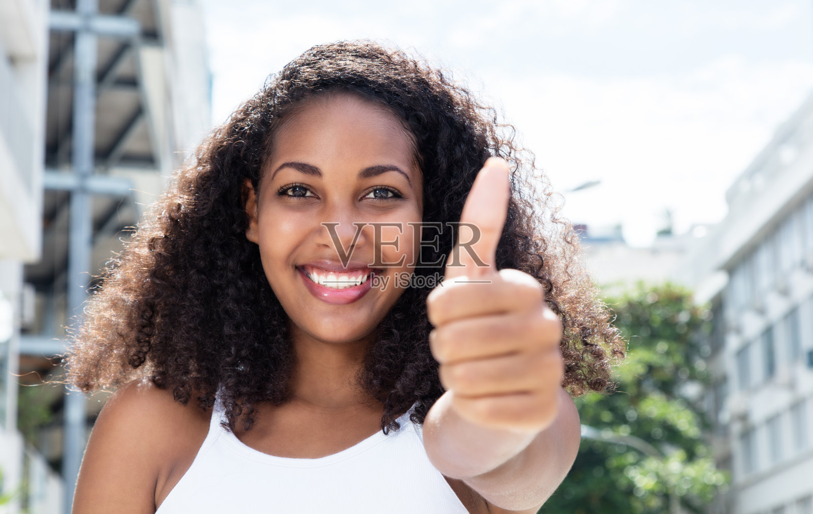 年轻的加勒比女人，一头卷发，在城市里露出拇指照片摄影图片