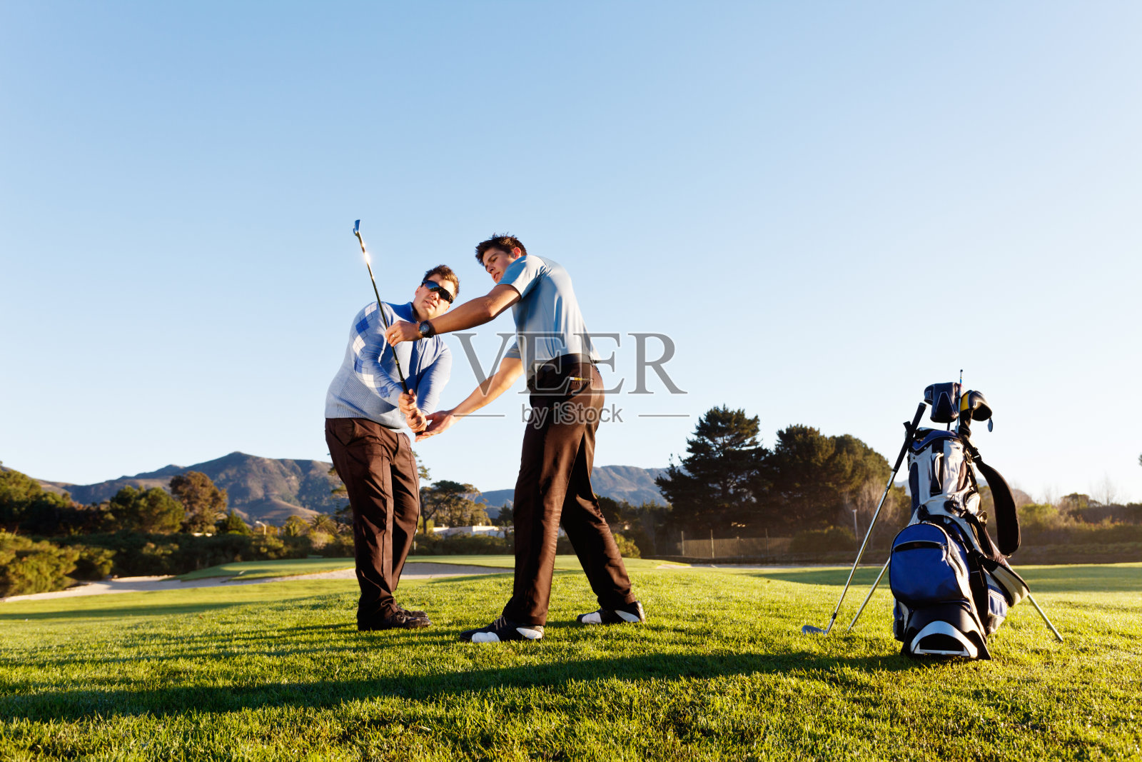 高尔夫课:年轻教练帮助高尔夫球手在美丽的高尔夫球场照片摄影图片