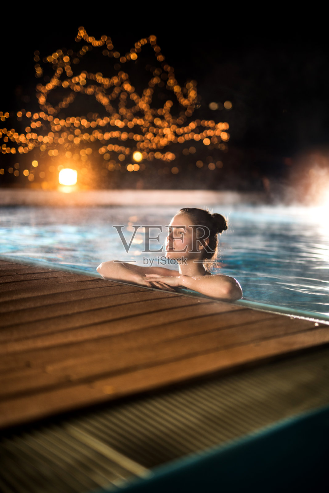 冬夜，年轻女子在热游泳池里放松。照片摄影图片