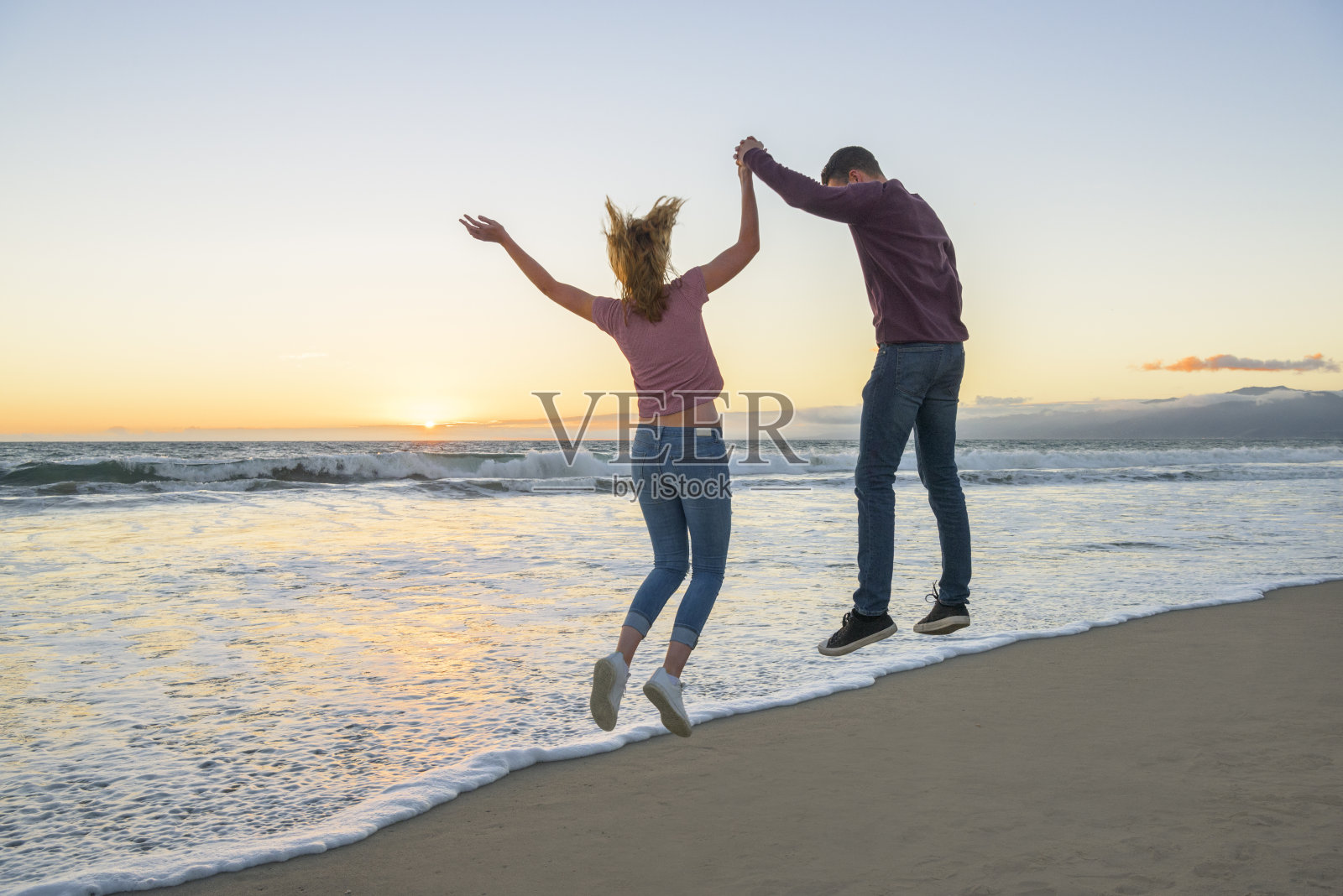 年轻夫妇手牵着手，在海滩上跳跃照片摄影图片