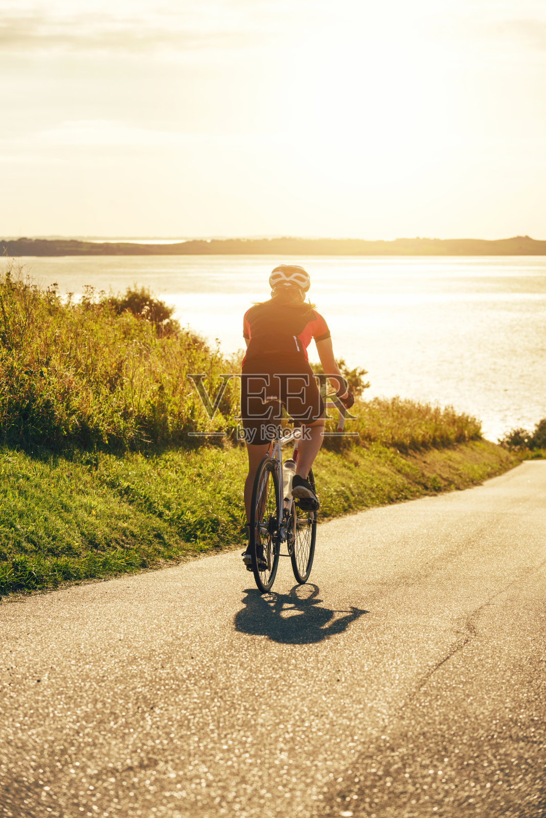 太阳下山时，骑自行车的人骑着自行车下山照片摄影图片