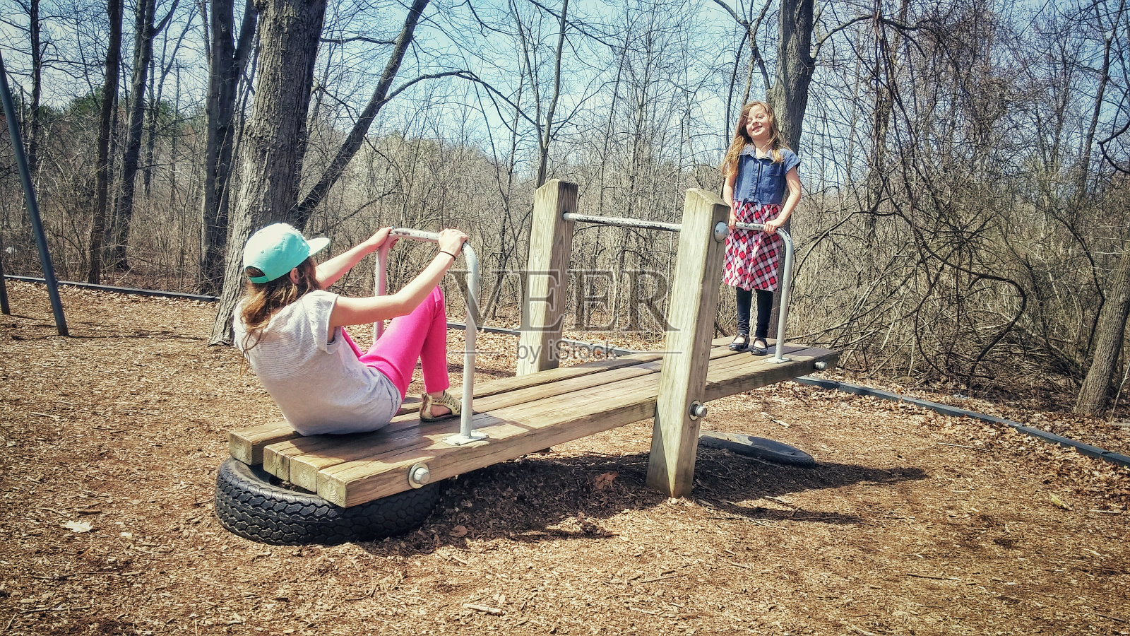 两个女孩在玩跷跷板，公园操场附近的森林照片摄影图片