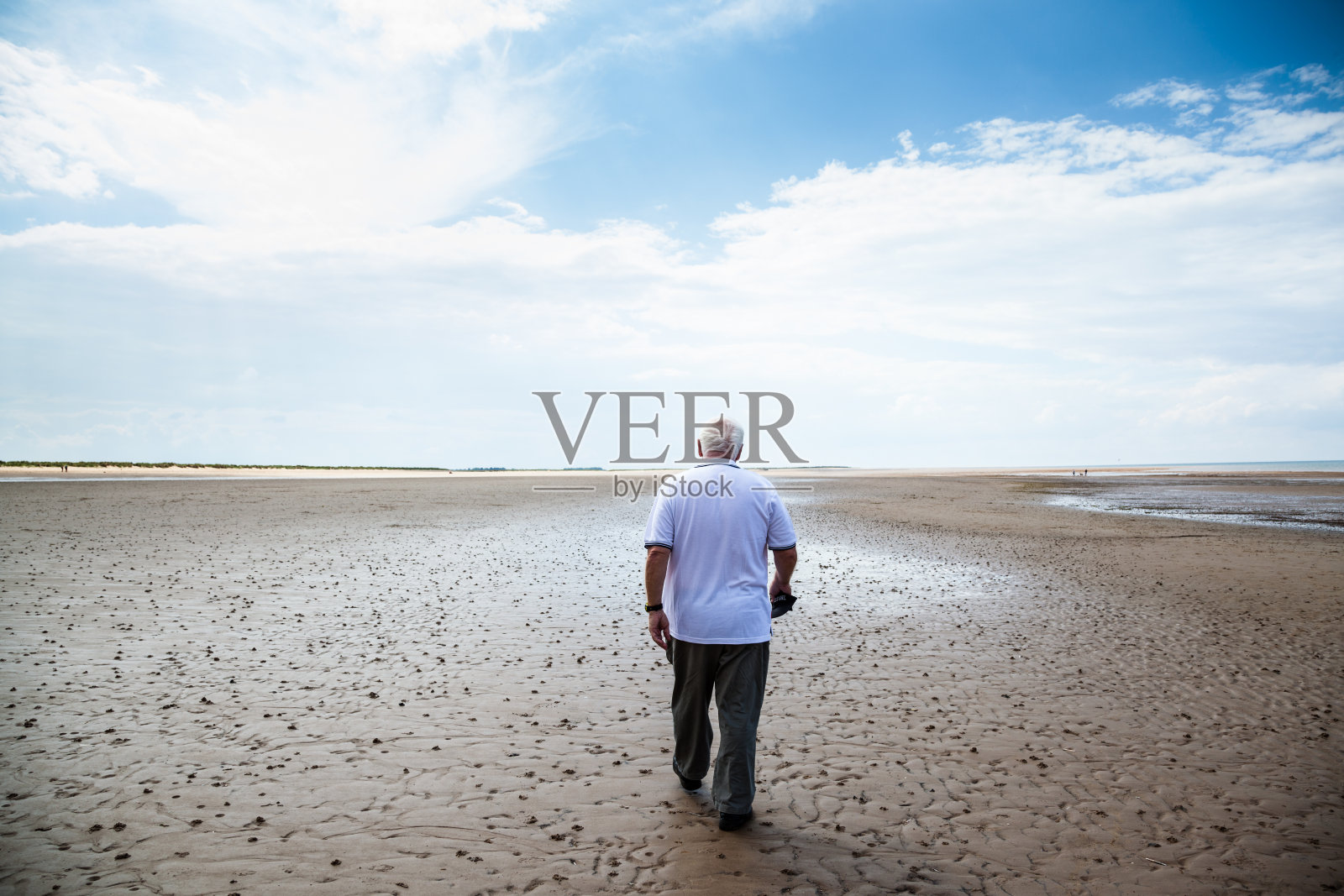在英格兰诺福克布兰克斯特，一位穿着白色t恤的老人走在空旷潮湿的海滩上照片摄影图片