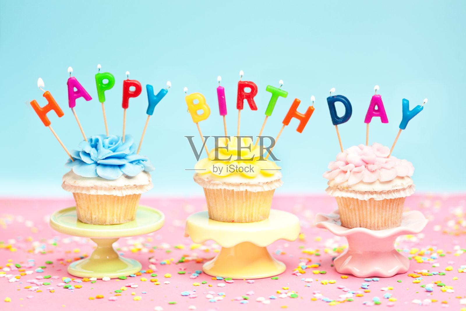 三个生日纸杯蛋糕，粉红背景上有蜡烛和五彩纸屑照片摄影图片