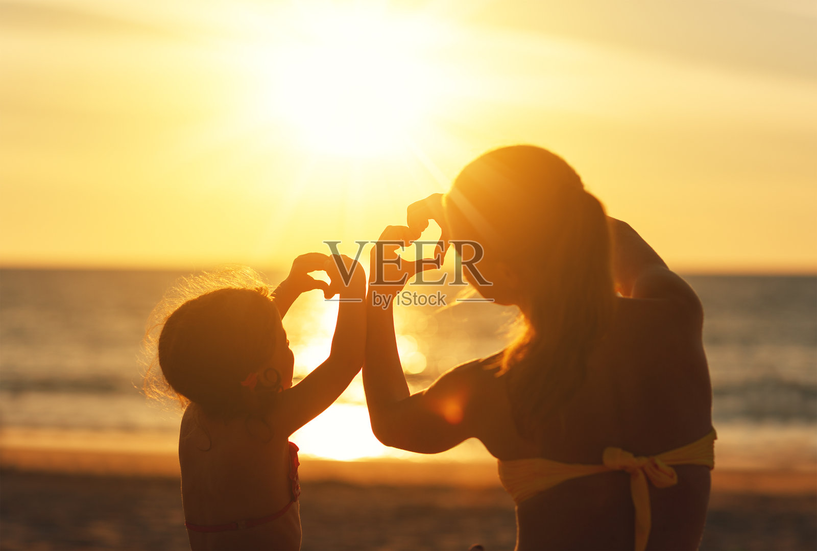 爱的概念，父母和幸福的家庭。母亲和孩子的女儿在日落时从手上露出心来照片摄影图片