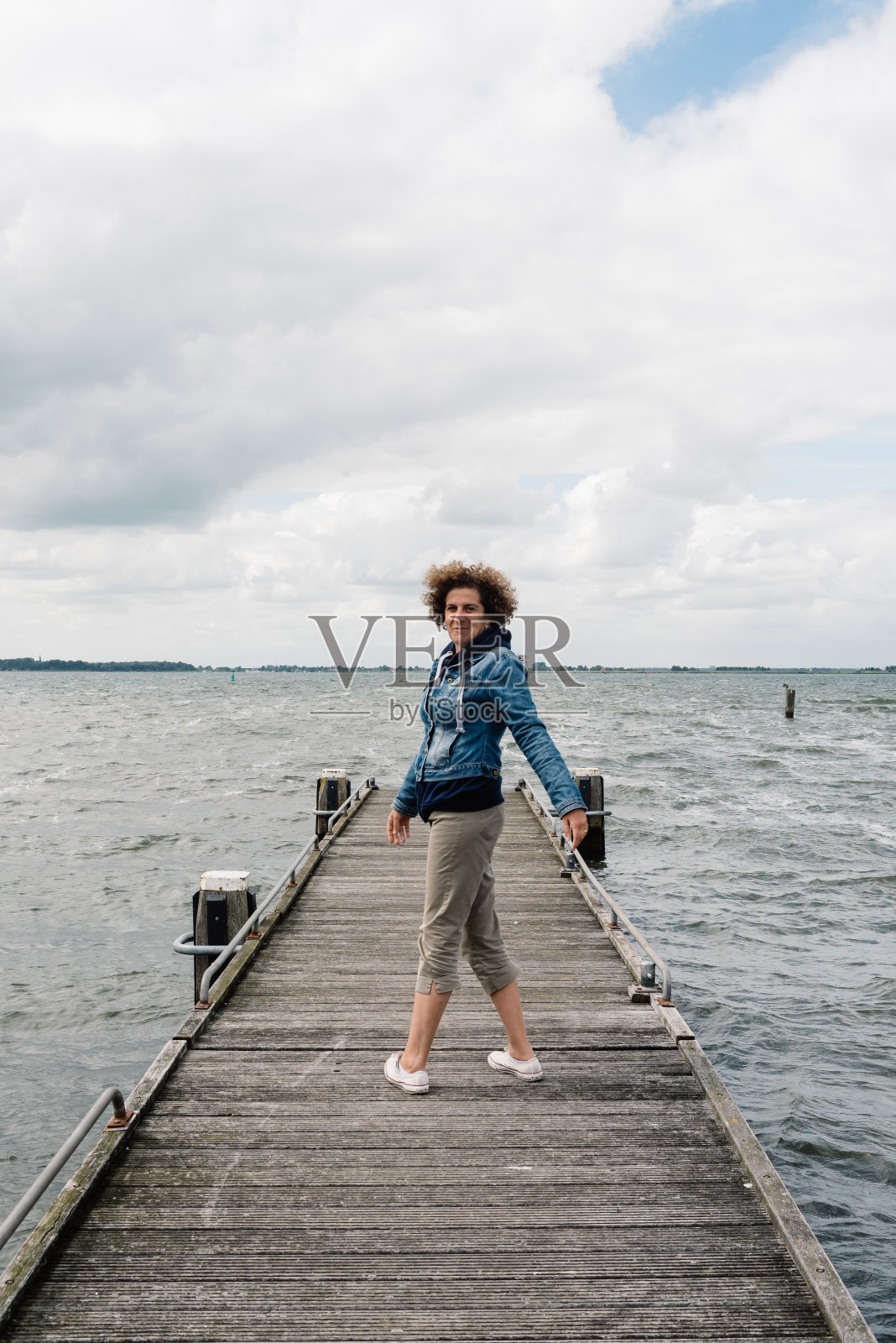 一个阴天的夏天，穿着休闲的女人站在木栈桥上。自由的概念照片摄影图片