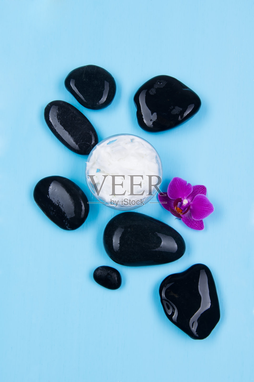 带着兰花香味的奶油被黑色的石头环绕在蓝色的背景上照片摄影图片
