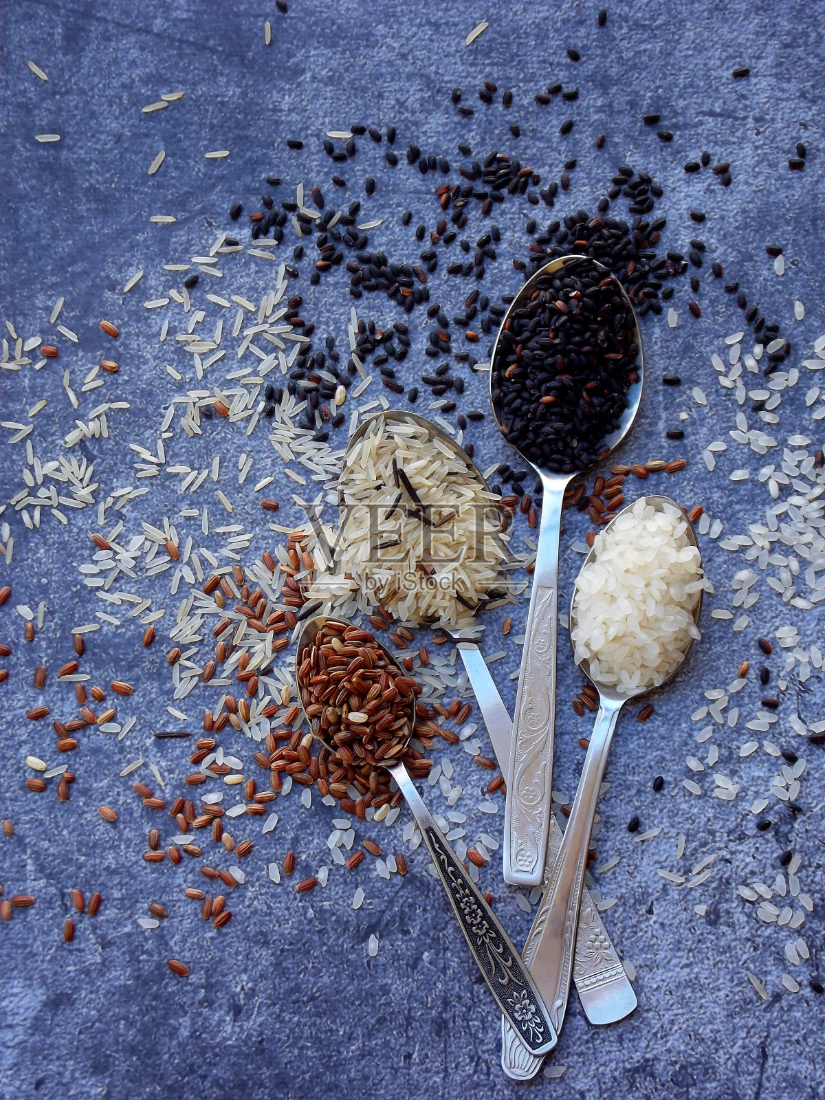 不同类型的大米在灰色的背景:白色糯米，黑色，印度香米，棕色和混合大米。健康的概念。前视图。副本的空间。照片摄影图片