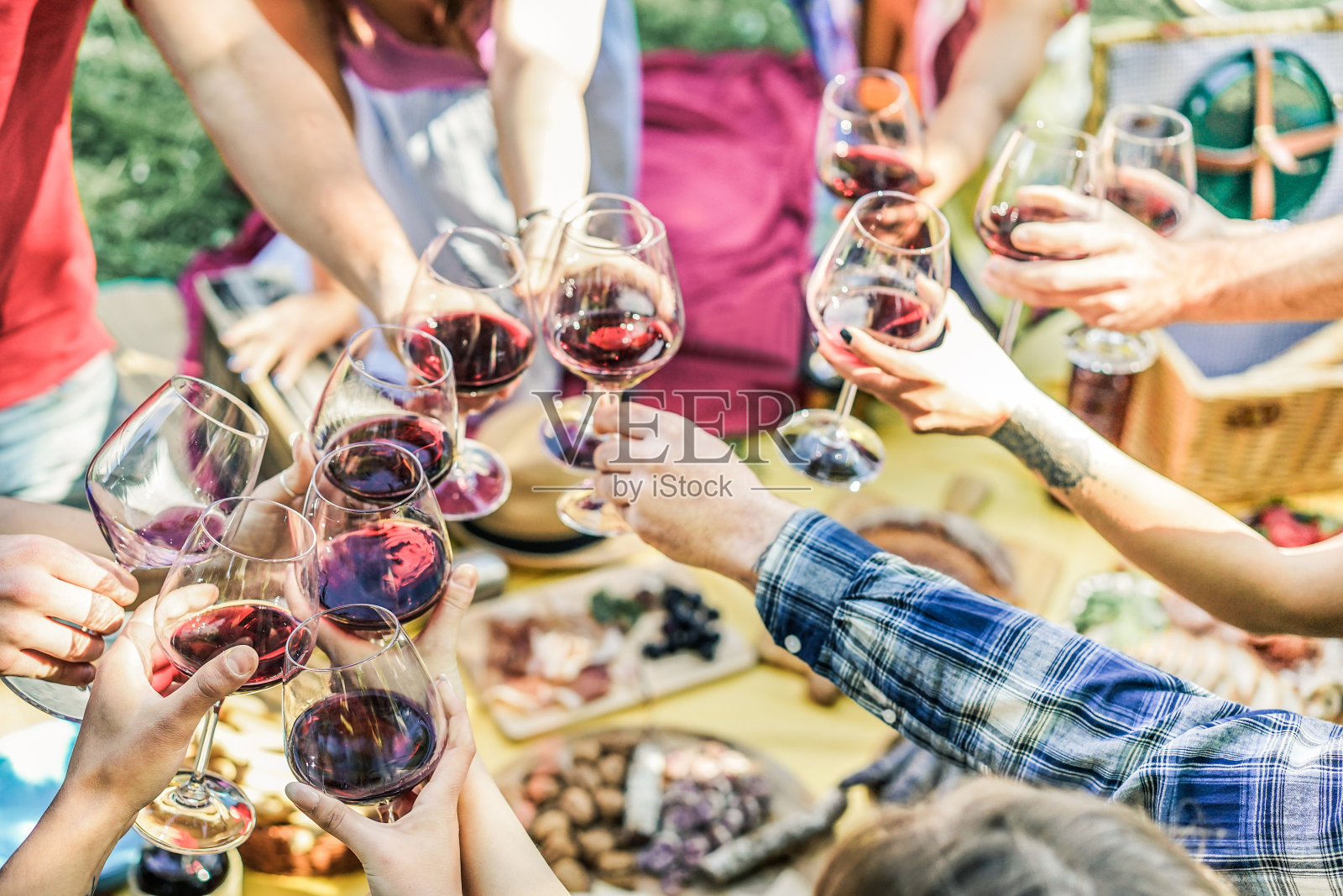 一群朋友享受野餐，同时喝红酒和吃小吃开胃菜户外-年轻人欢呼和有乐趣在一起-关注右下角的手玻璃杯-古董过滤器照片摄影图片