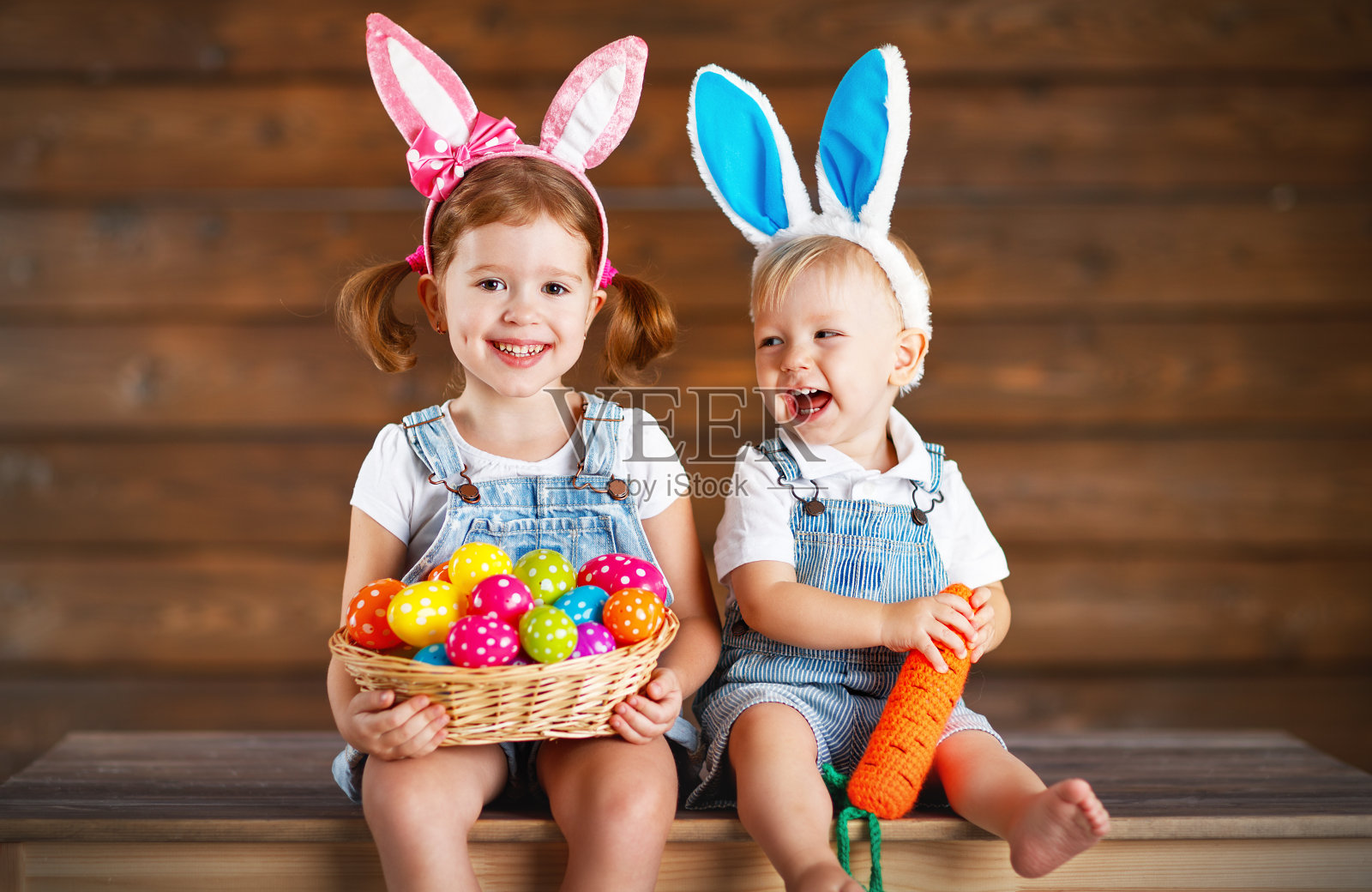快乐的孩子们，男孩和女孩装扮成复活节兔子，用一篮子的鸡蛋放在木头上照片摄影图片