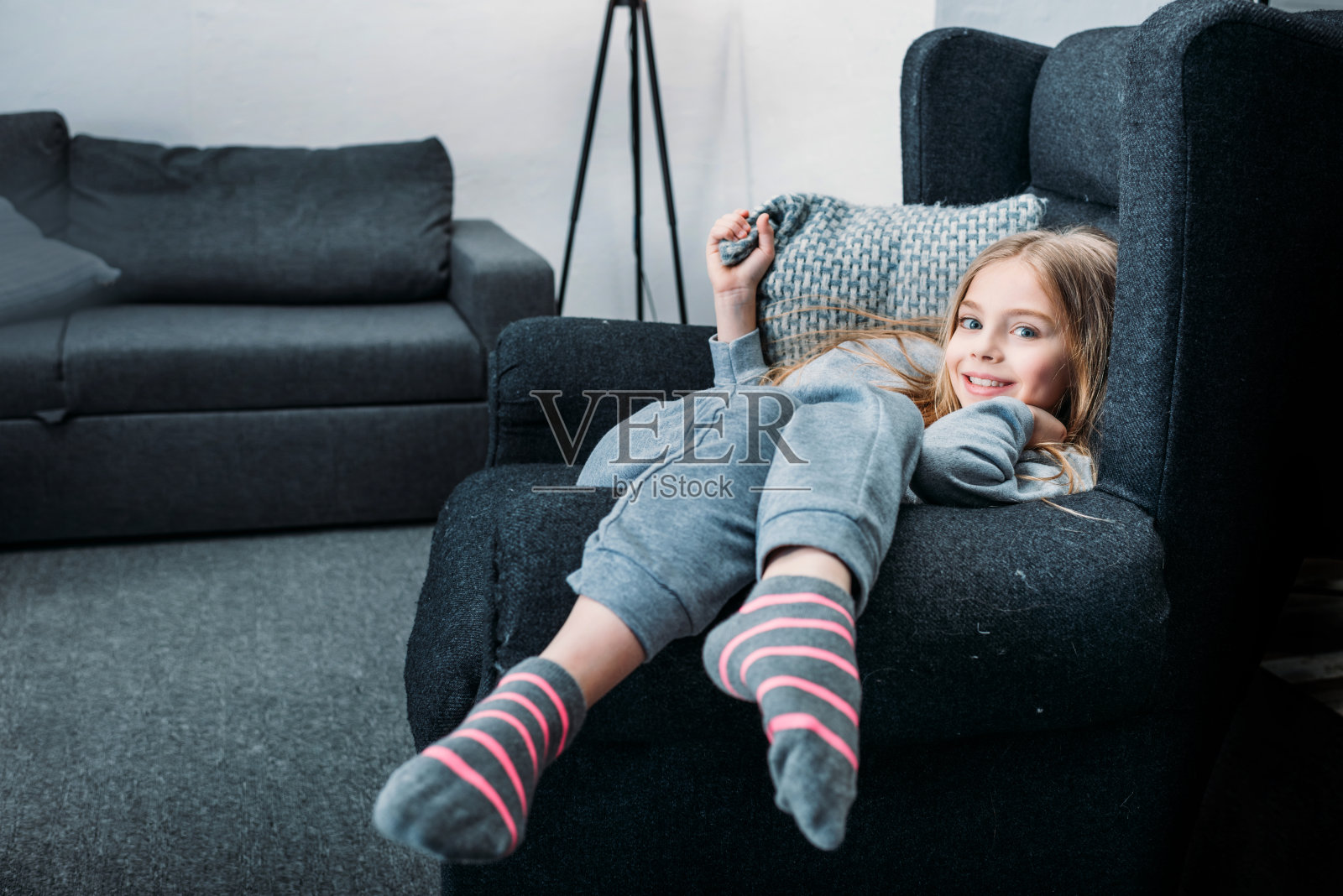 微笑的小女孩躺在扶手椅和枕头，看着相机照片摄影图片