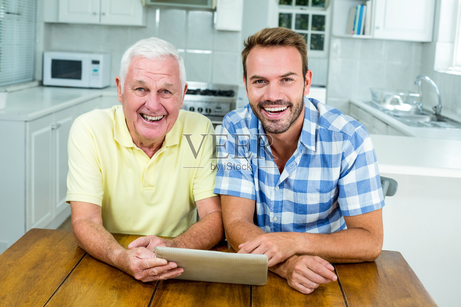 快乐的父亲和儿子在厨房的桌子上使用数字平板电脑照片摄影图片