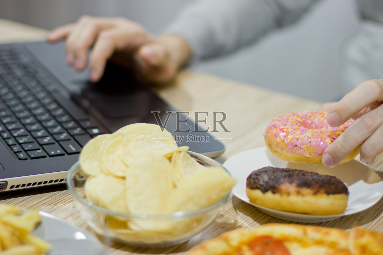一个人在电脑前工作，吃快餐。不健康食品:汉堡，酱汁，土豆，甜甜圈，薯条。照片摄影图片