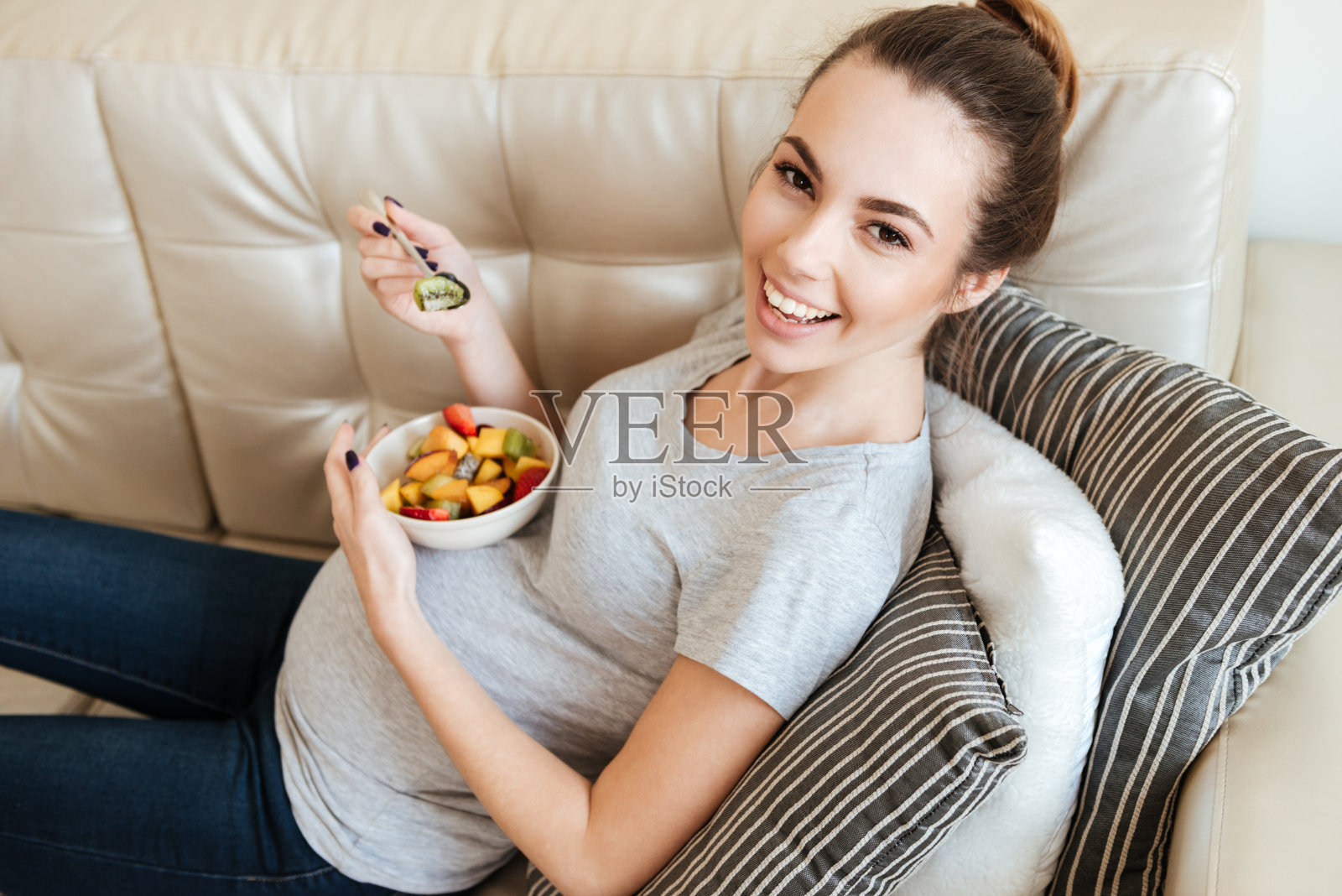 快乐的孕妇坐在沙发上吃水果沙拉照片摄影图片