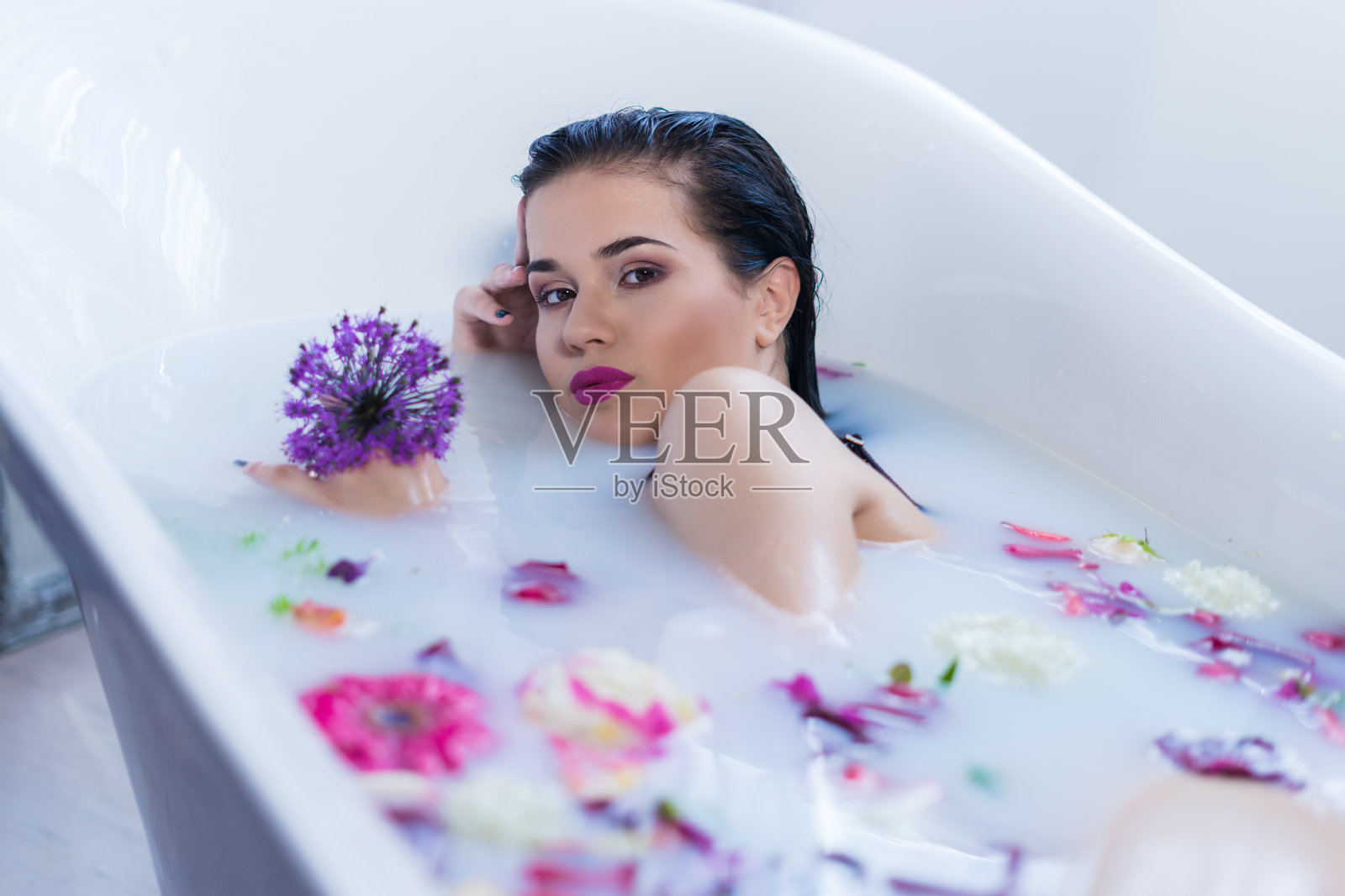 性感的黑发女人放松在一个热浴与鲜花照片摄影图片