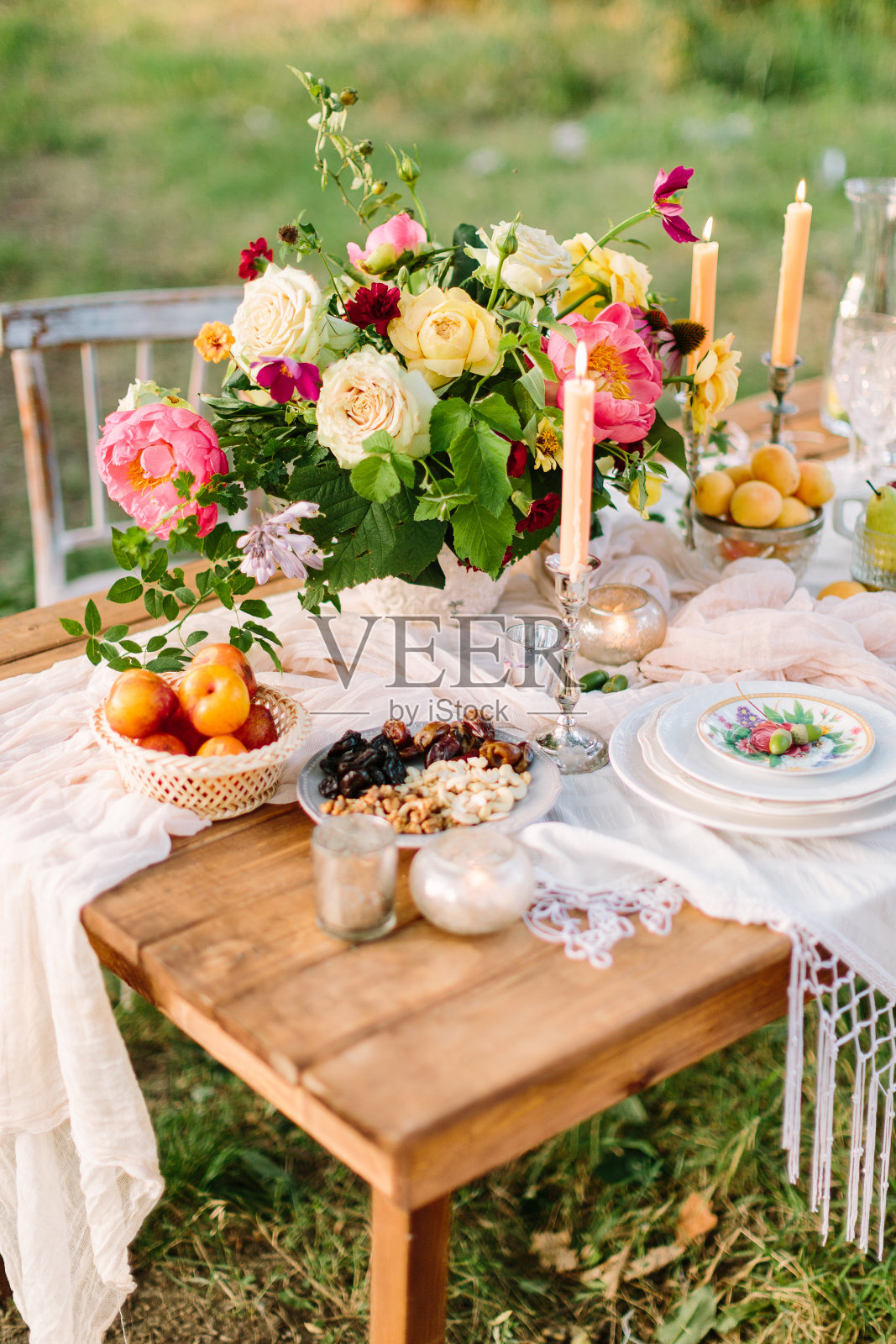 浪漫、爱情、婚礼、假日、装饰、休息概念——浪漫的餐桌布置，中间点缀着鲜艳的五彩花束，白色的宴席餐具，细长的蜡烛，水果和坚果照片摄影图片