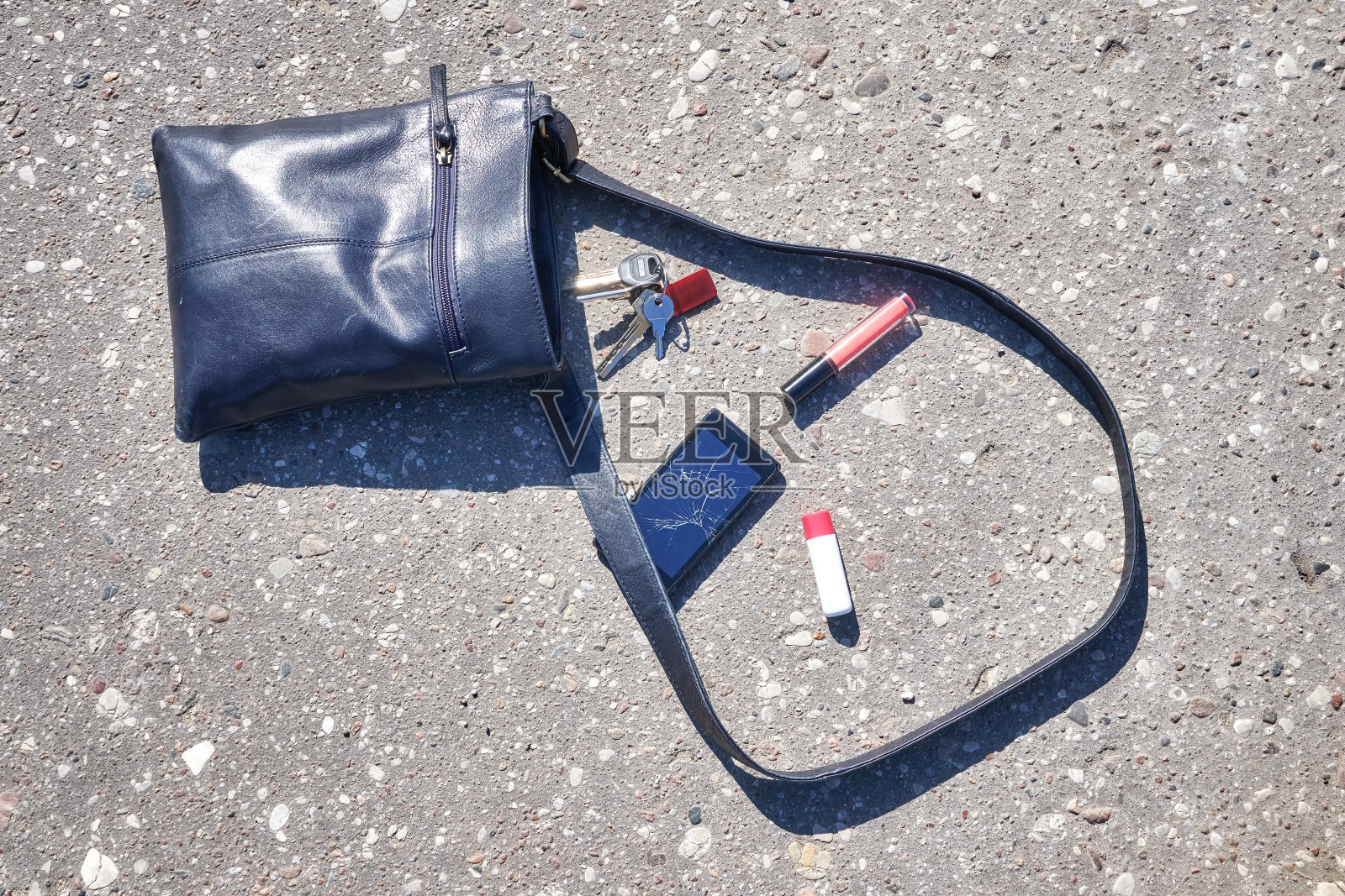 手提包，坏掉的手机，钥匙和口红在柏油路上。照片摄影图片