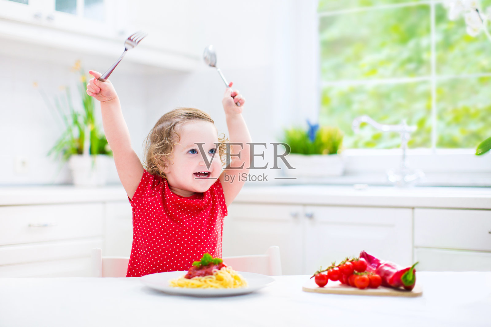 可爱的蹒跚学步的小女孩玩着叉子和勺子吃意大利面照片摄影图片