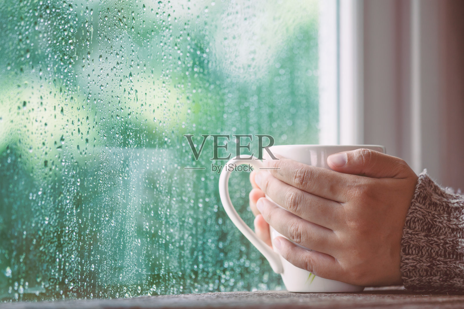 女人手拿着一杯咖啡或茶在雨天的窗户背景照片摄影图片
