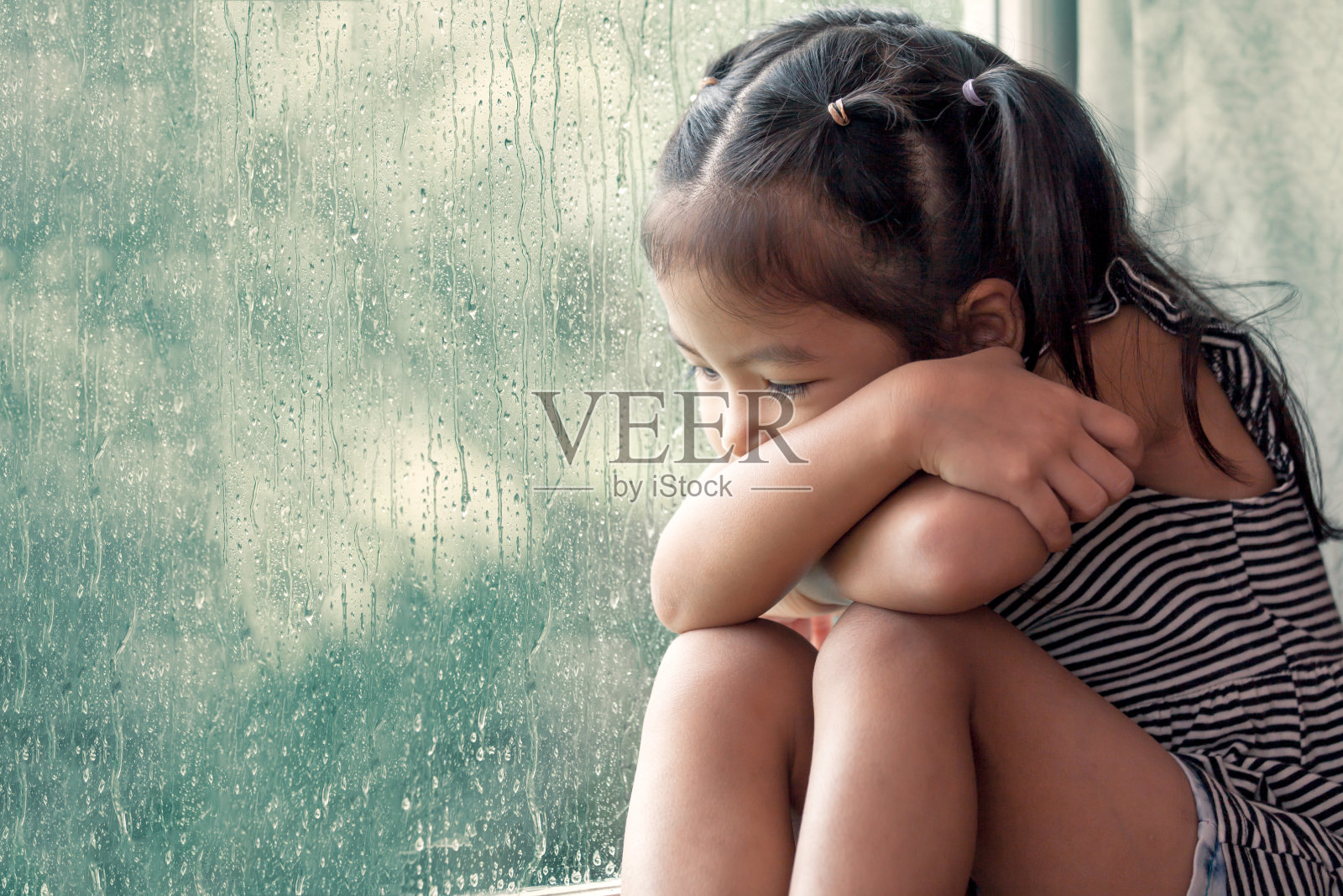 悲伤的亚洲小女孩望着窗外在雨天照片摄影图片