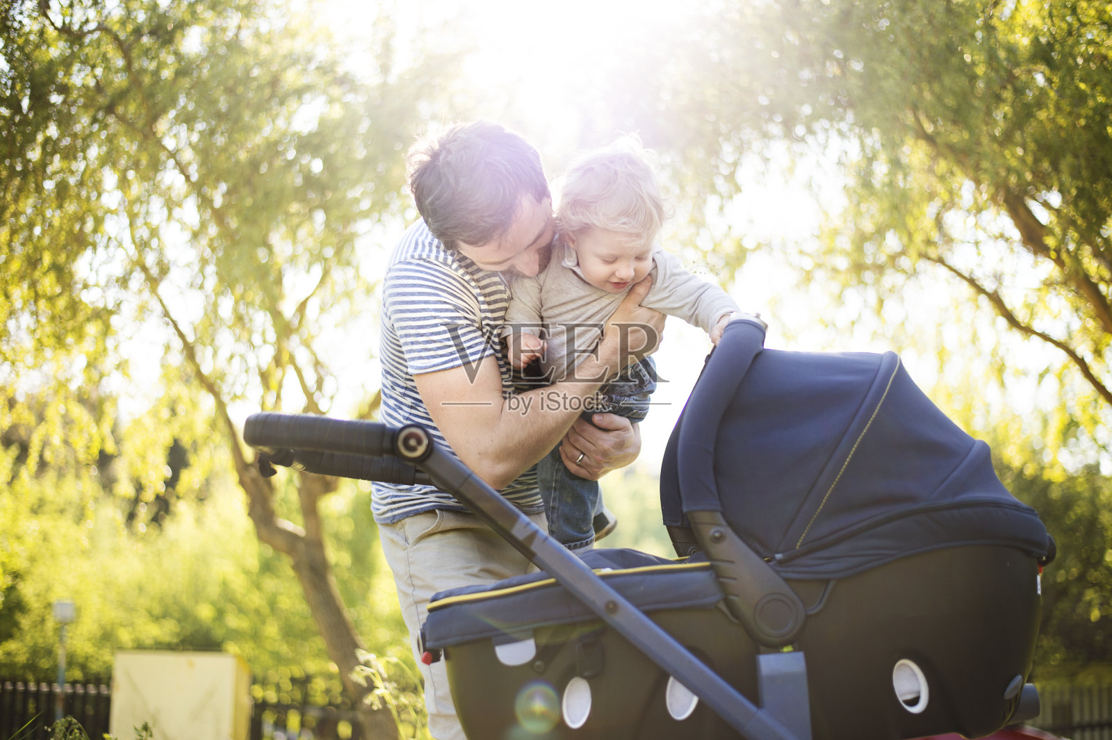 父亲推着婴儿车带着小儿子和小女儿。阳光明媚的公园。照片摄影图片