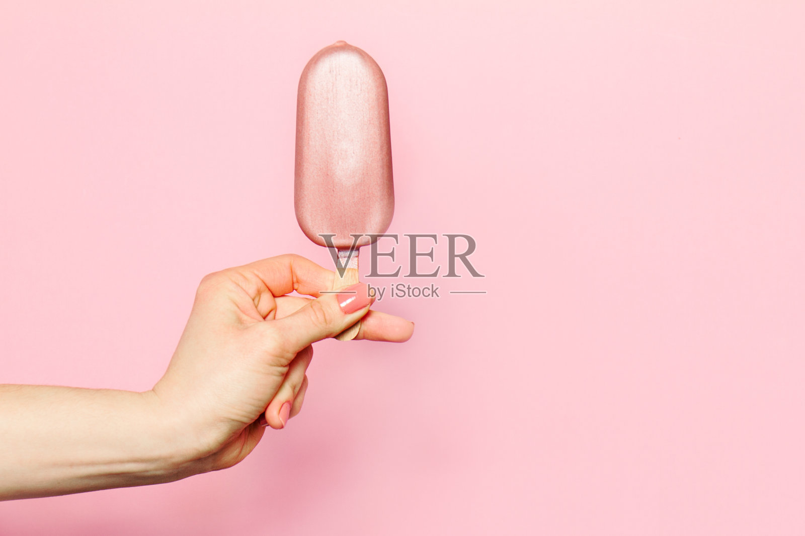 一个年轻女子的手拿着冰淇淋在粉红色的背景。照片摄影图片
