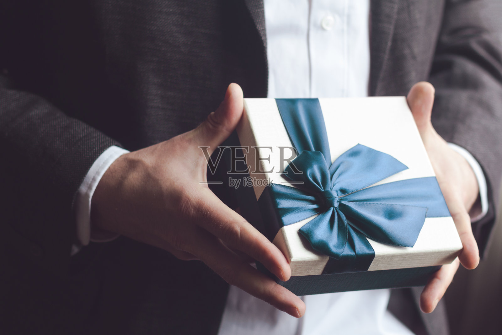 西装男献上带着蓝丝带的礼物照片摄影图片