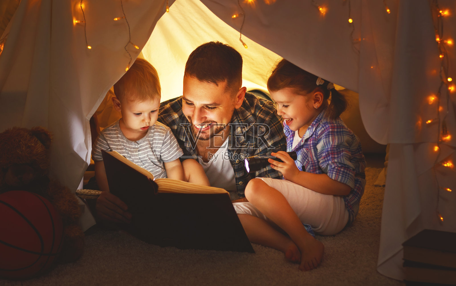 快乐的家庭，爸爸和孩子们在家里的帐篷里看书照片摄影图片