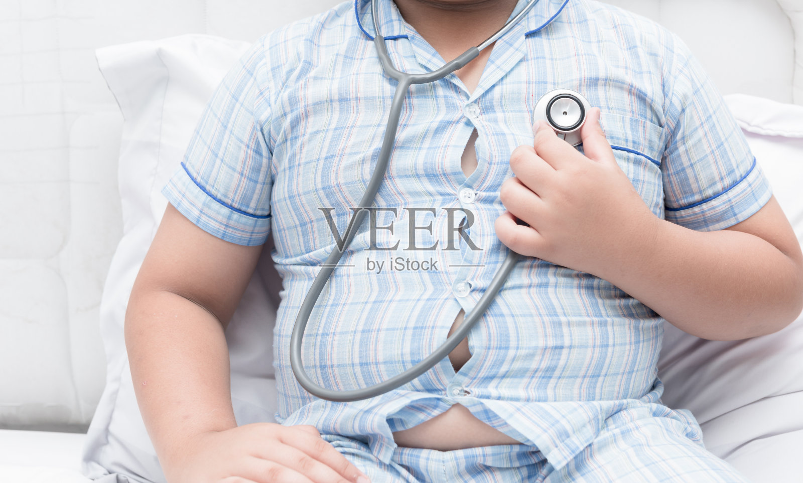 肥胖的胖男孩用听诊器检查心脏。照片摄影图片