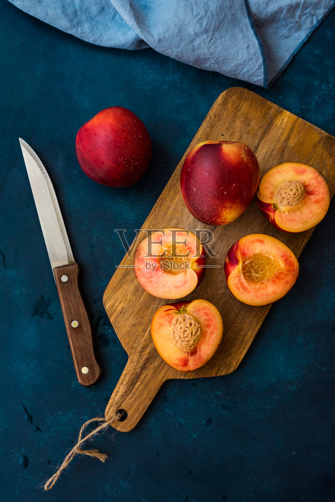 熟透多汁的油桃，切成两半，放在木板上，用刀切，深蓝色背景，俯视图，平铺，极简风格照片摄影图片