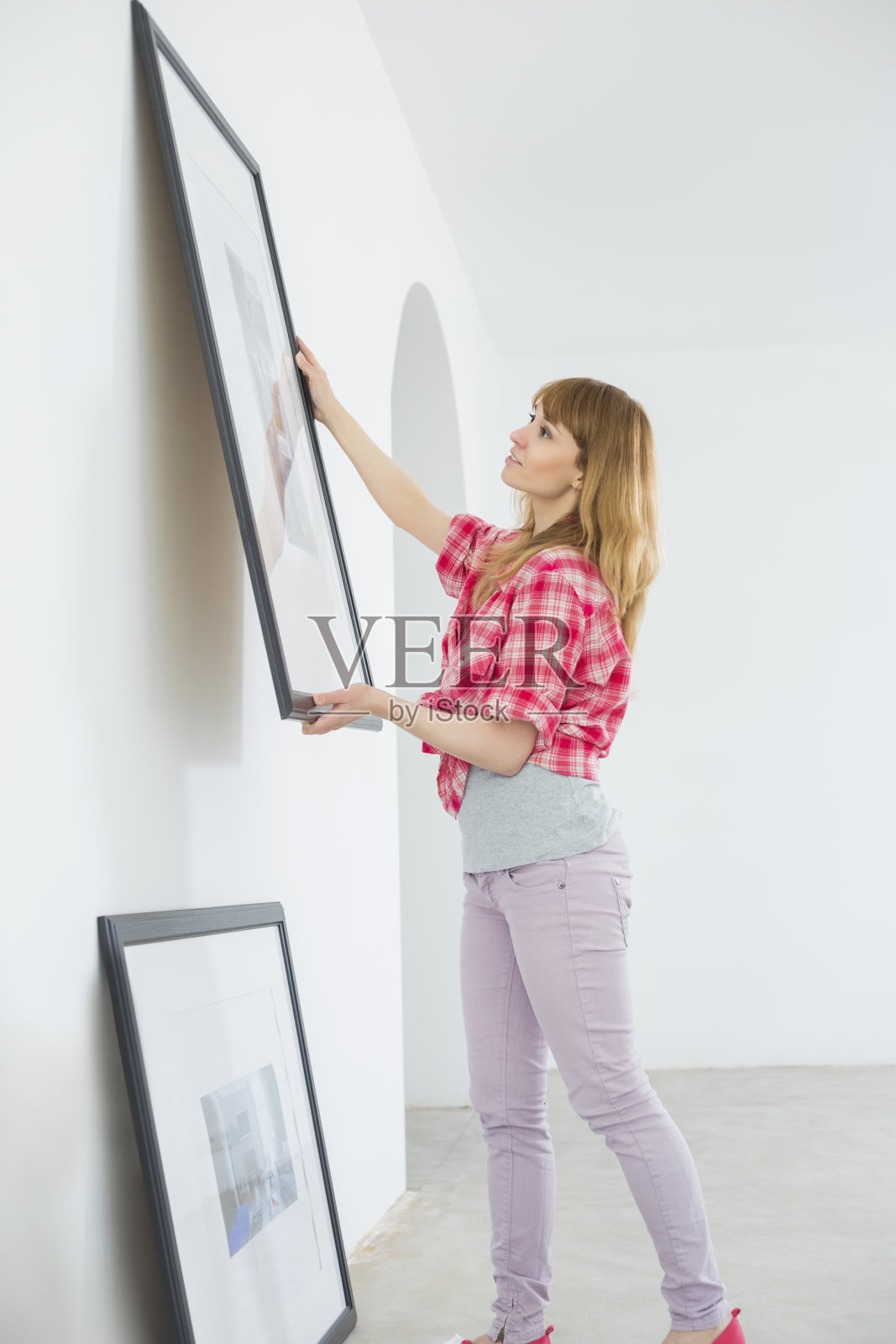 一个女人在新房子的墙上挂画框照片摄影图片
