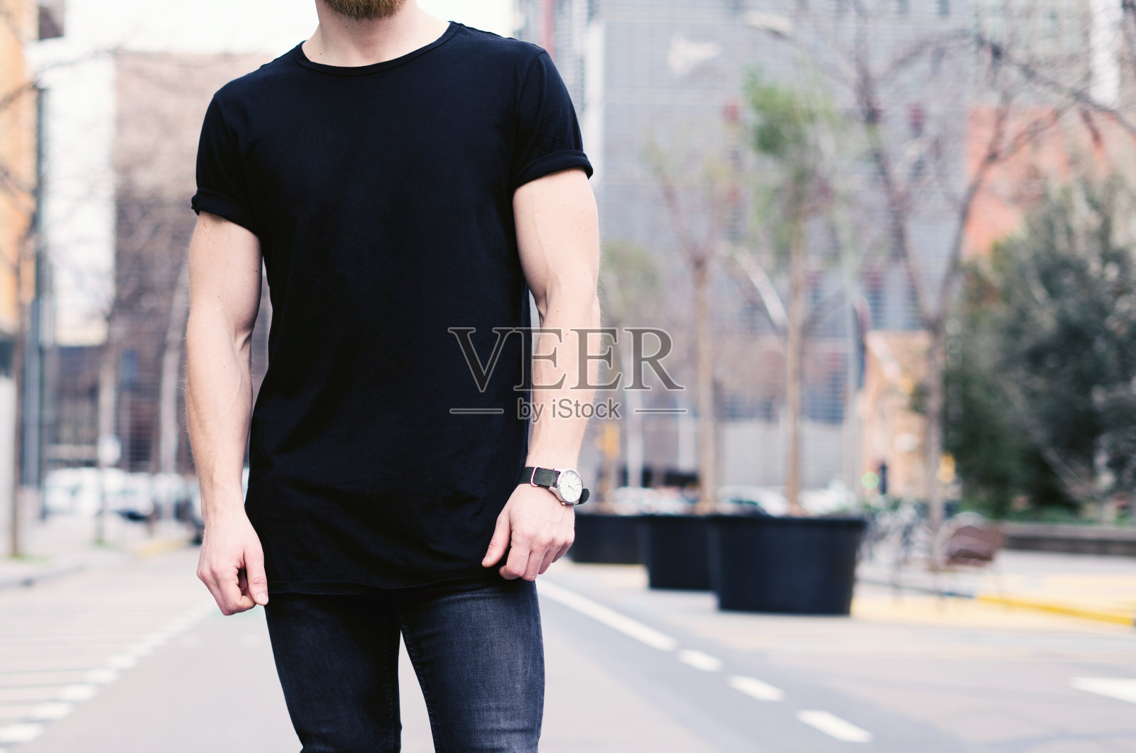 年轻肌肉男穿着黑色t恤和牛仔裤在现代城市的街道摆姿势的特写。模糊的背景。Hotizontal模型。照片摄影图片