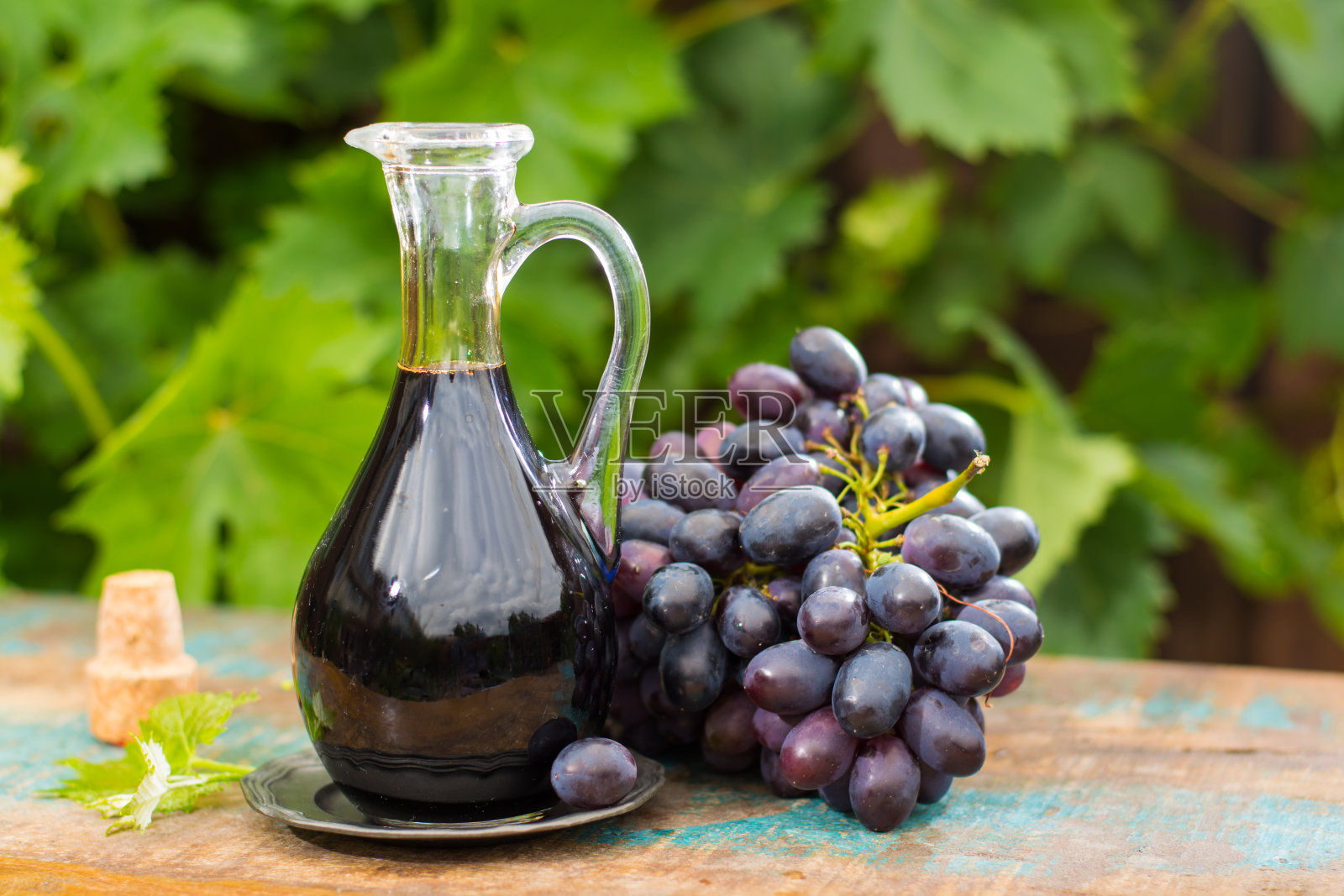 黑旧香醋在一个玻璃罐子与新鲜的红葡萄在绿色葡萄园的背景照片摄影图片