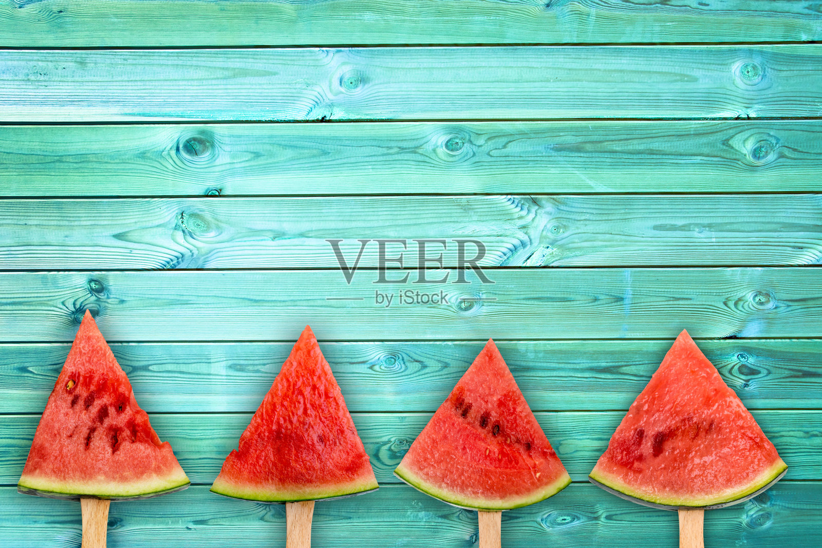 四个西瓜切片冰棒在蓝色木材背景与拷贝空间，新鲜的夏季水果概念照片摄影图片
