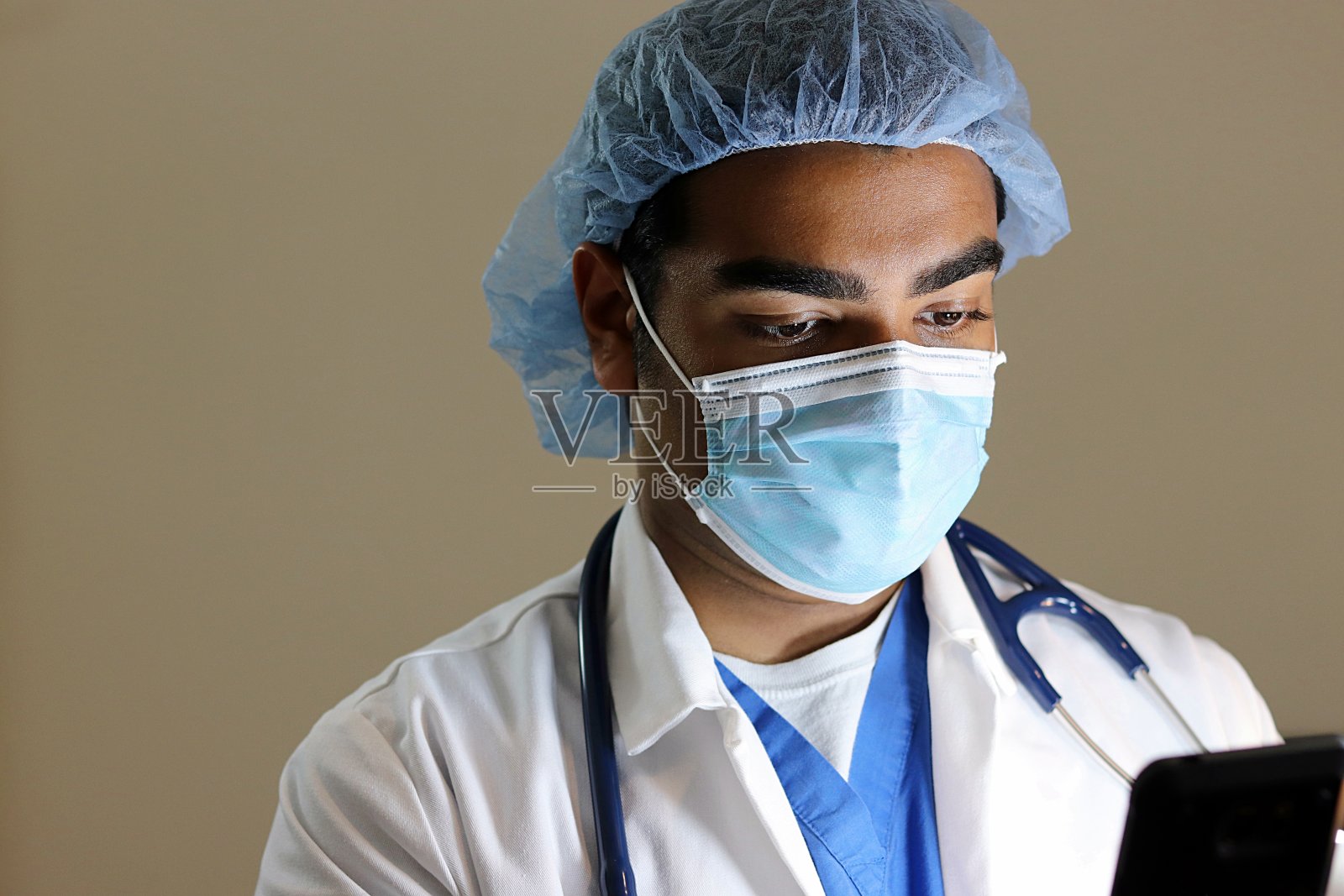 年轻英俊的医生穿着蓝色的手术服低头看手机照片摄影图片