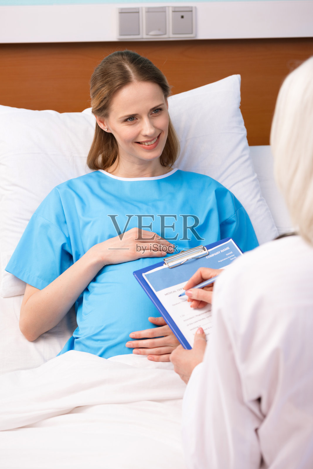 微笑孕妇摸着肚子，看着医生在写字板上写字照片摄影图片