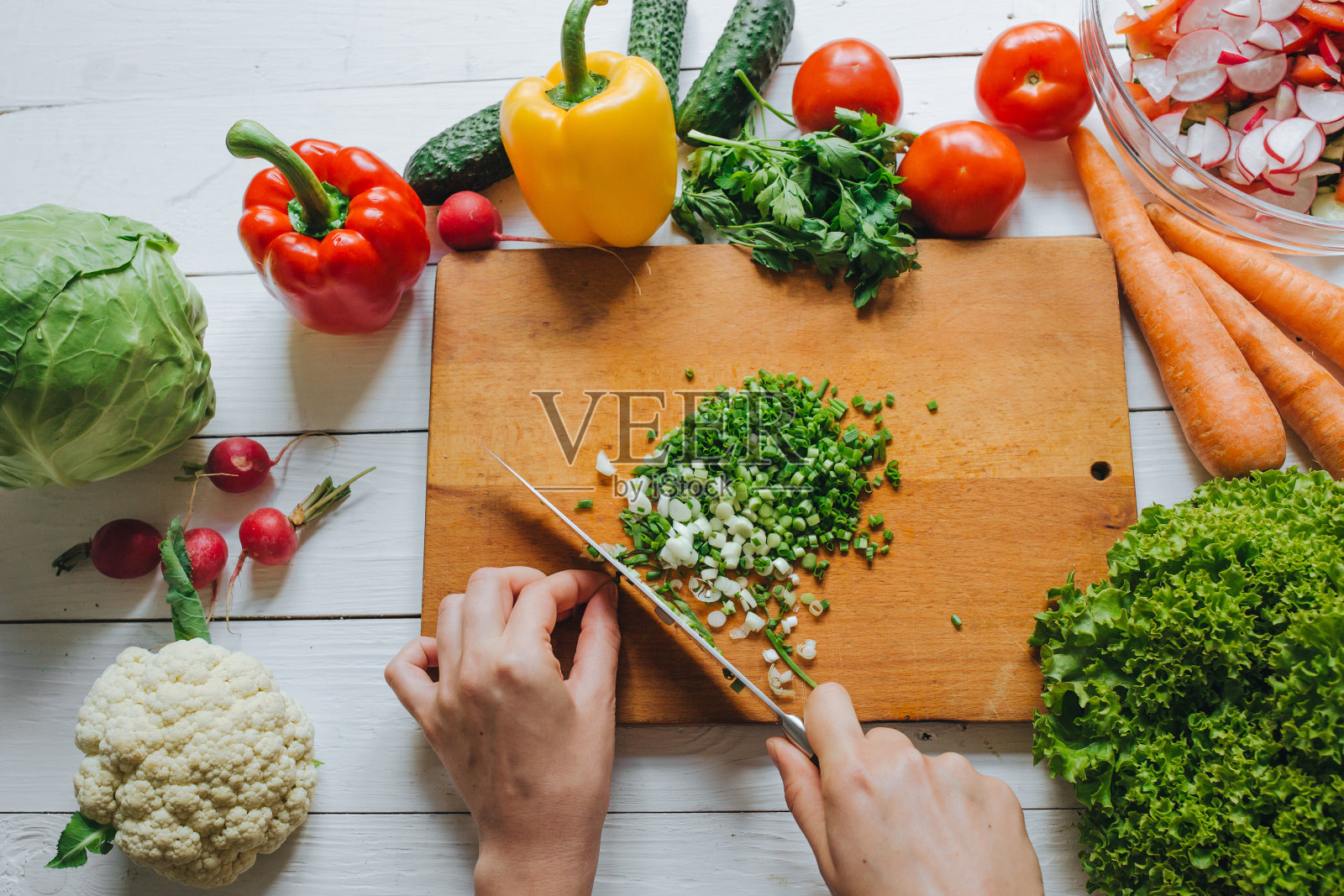 女人用手在头顶的木板上切新鲜的绿洋葱。白色背景。健康的烹饪概念。蔬菜。照片摄影图片