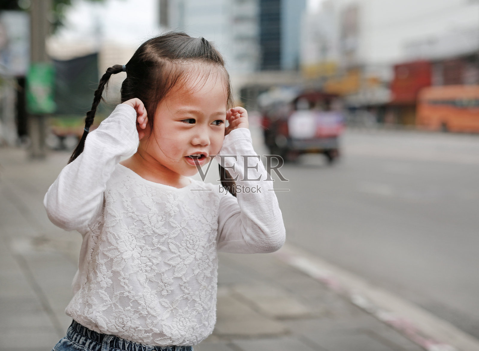 可爱的小女孩闭上耳朵，捂着双手捂着耳朵不听。照片摄影图片