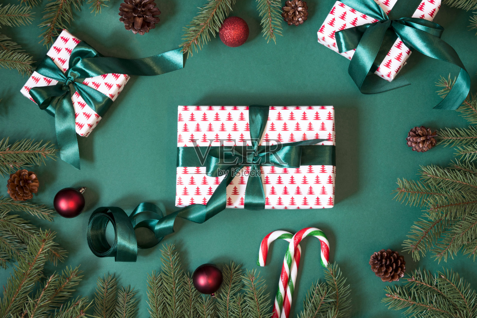 圣诞礼盒和礼物包装在设计纸和绿色丝带在绿色与红色装饰。前视图。照片摄影图片