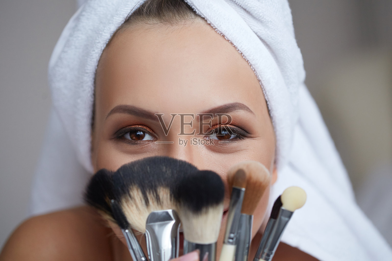 年轻美丽微笑的女人，头上戴着毛巾，手里拿着化妆刷。照片摄影图片