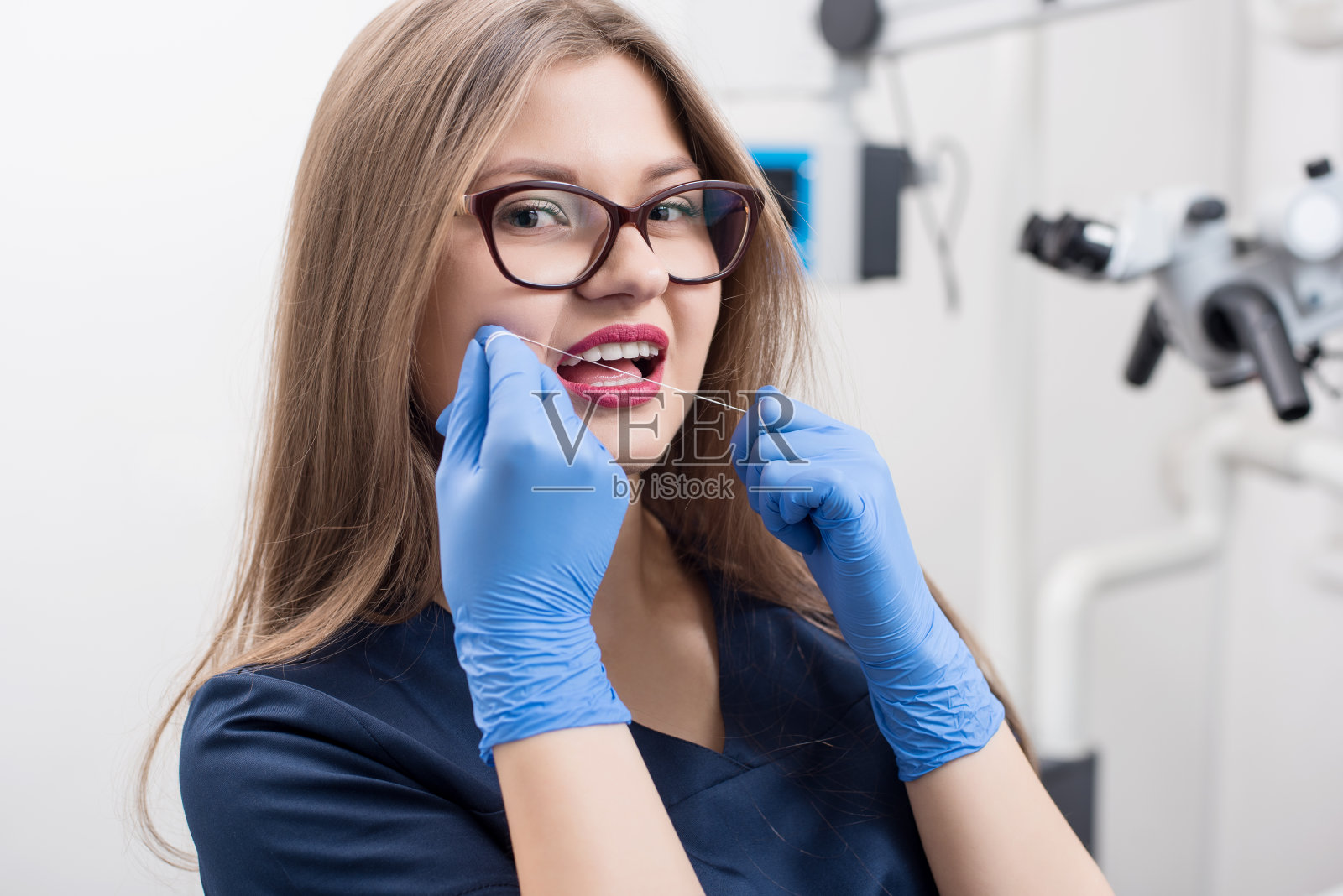 年轻美丽的女牙医与牙线在牙科诊所的特写。医生穿着蓝色制服，戴着手套和眼镜。牙医。口腔修复设备照片摄影图片