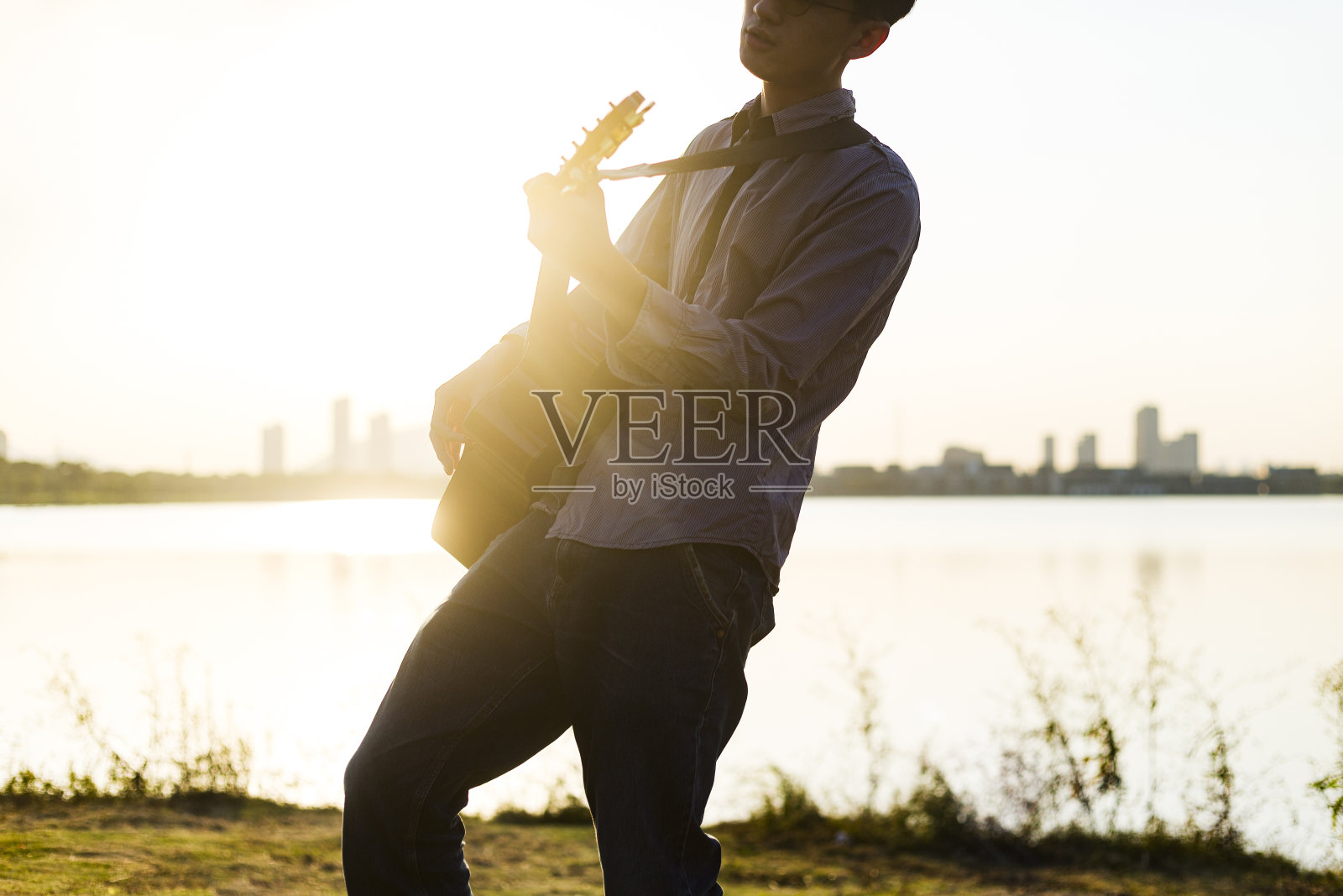 年轻男子在夕阳下弹奏吉他照片摄影图片