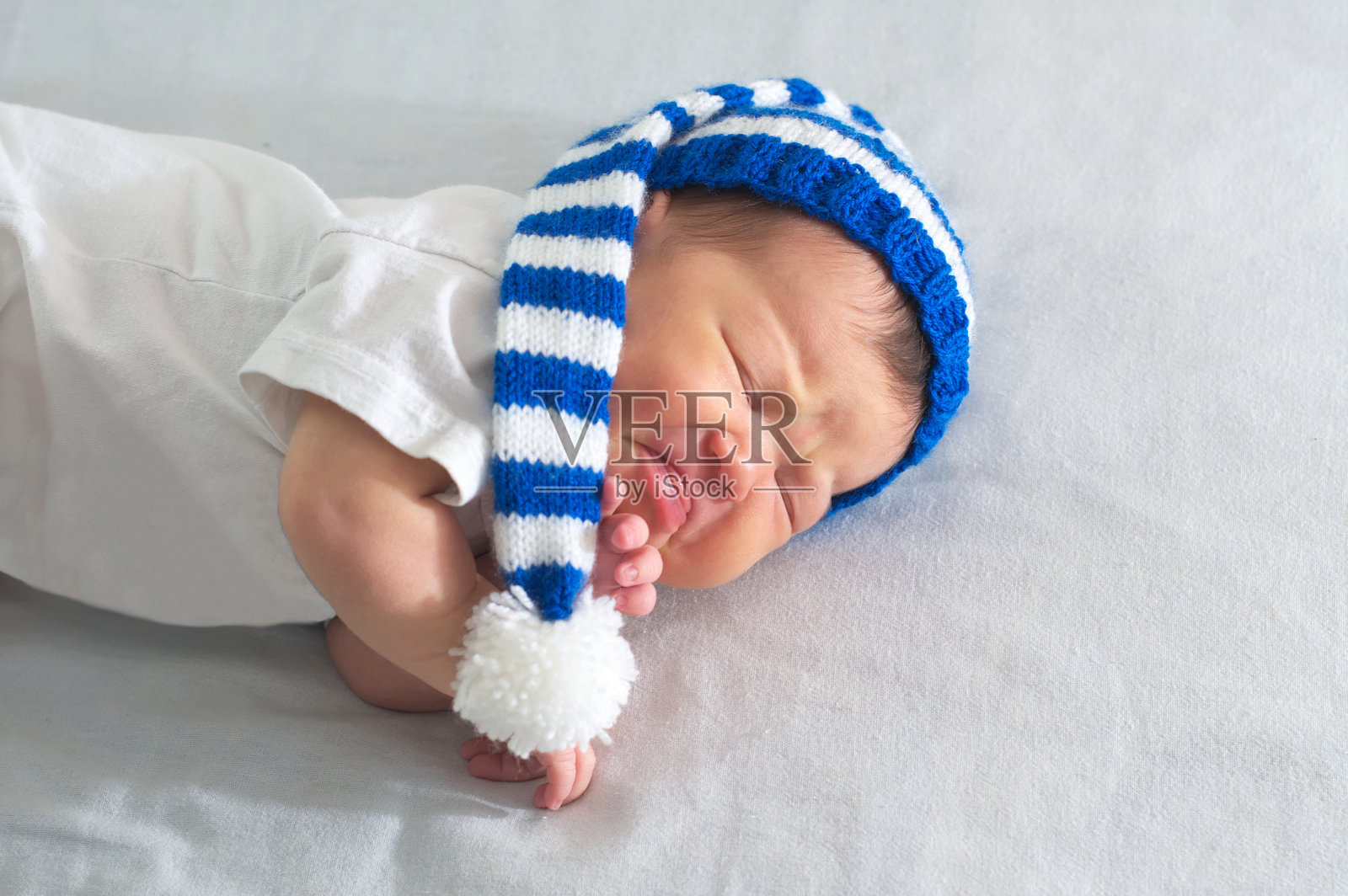 新生儿戴着帽子戴着白毯子，亚洲宝宝肚子疼。婴儿护理，出牙痛，腹痛照片摄影图片