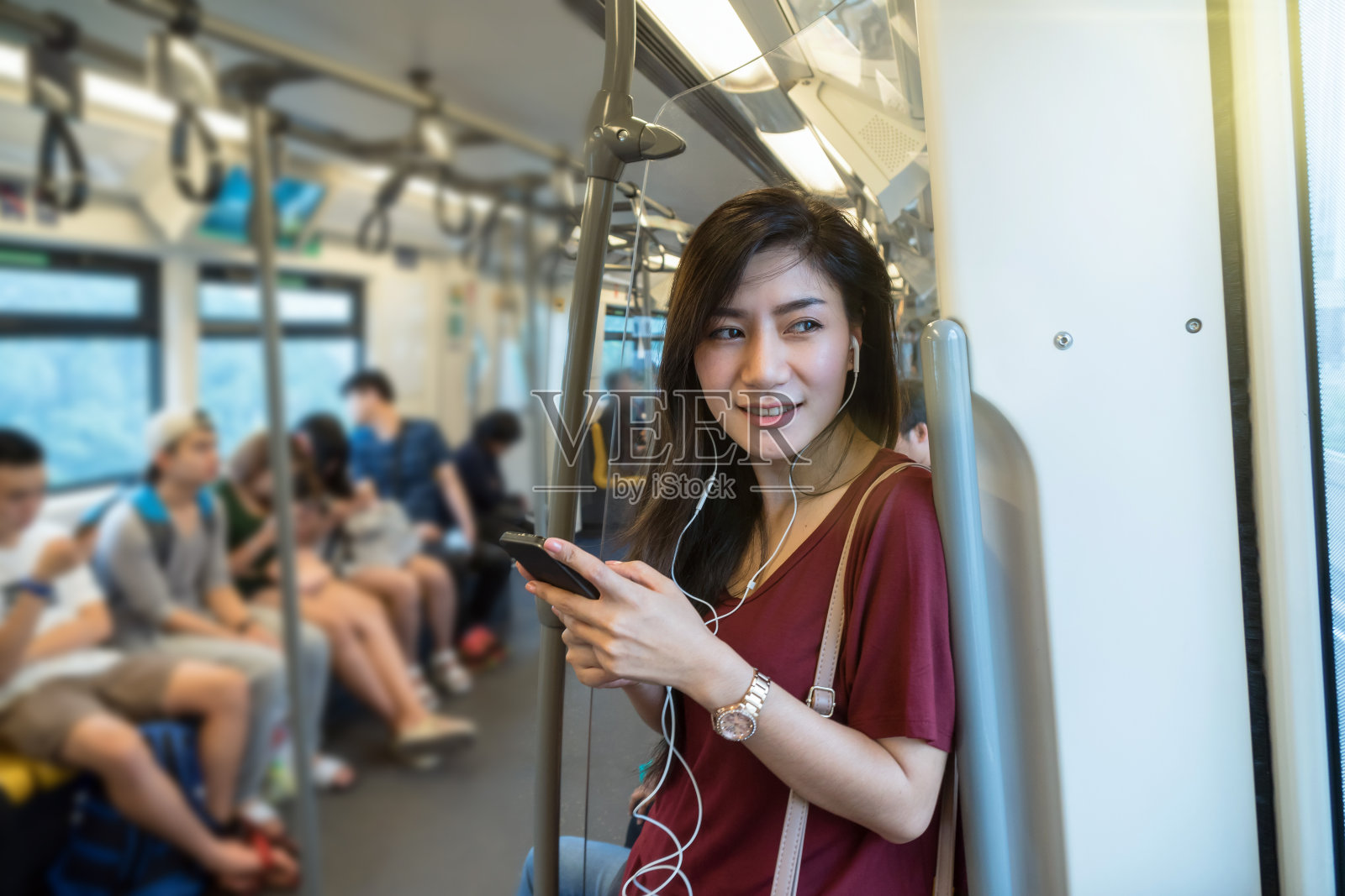 亚洲女性乘客穿休闲装使用和听歌曲通过智能手机在轻轨或地铁在大城市旅行，生活方式和交通理念照片摄影图片