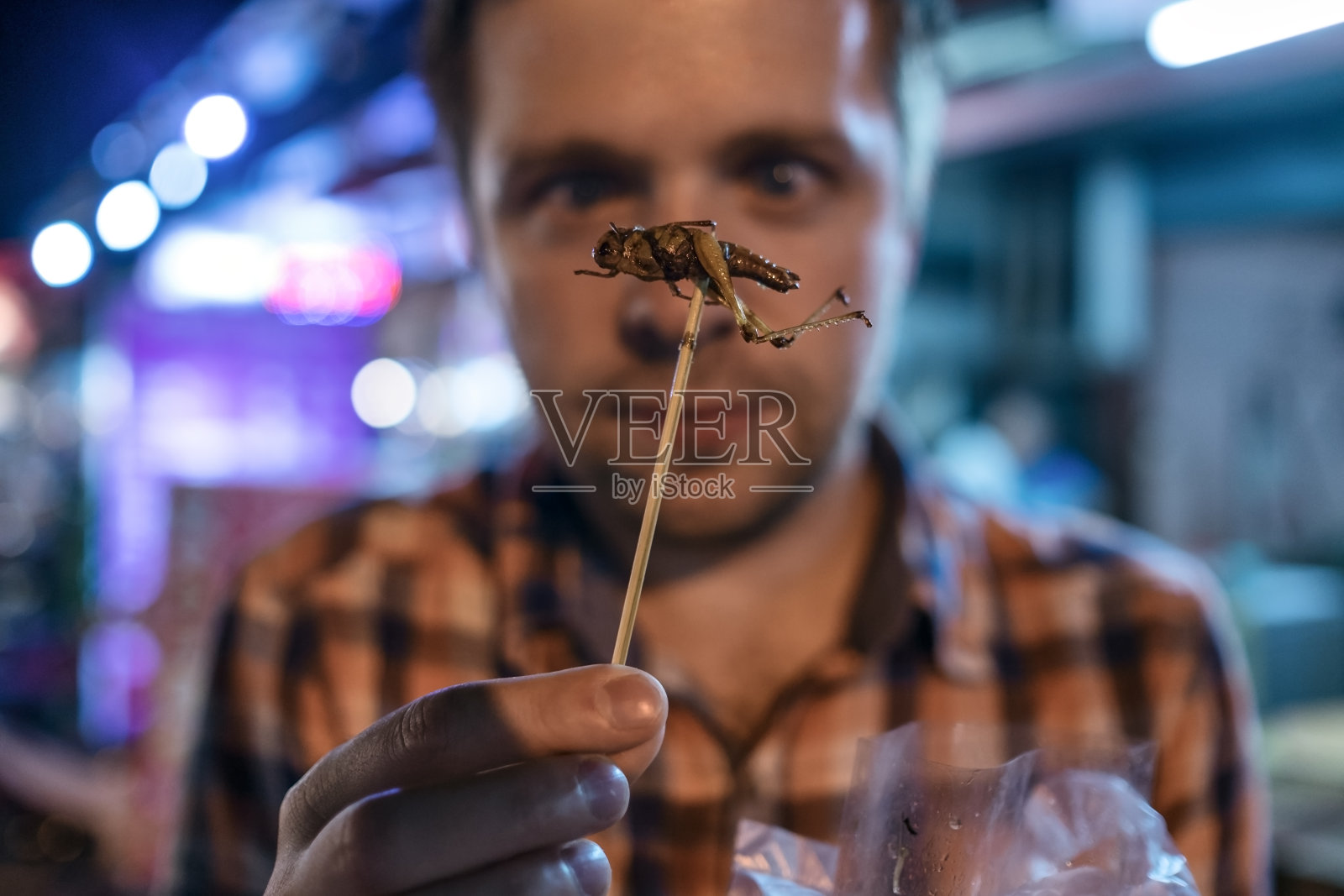 泰国夜市上吃蟋蟀的白人年轻男子。照片摄影图片